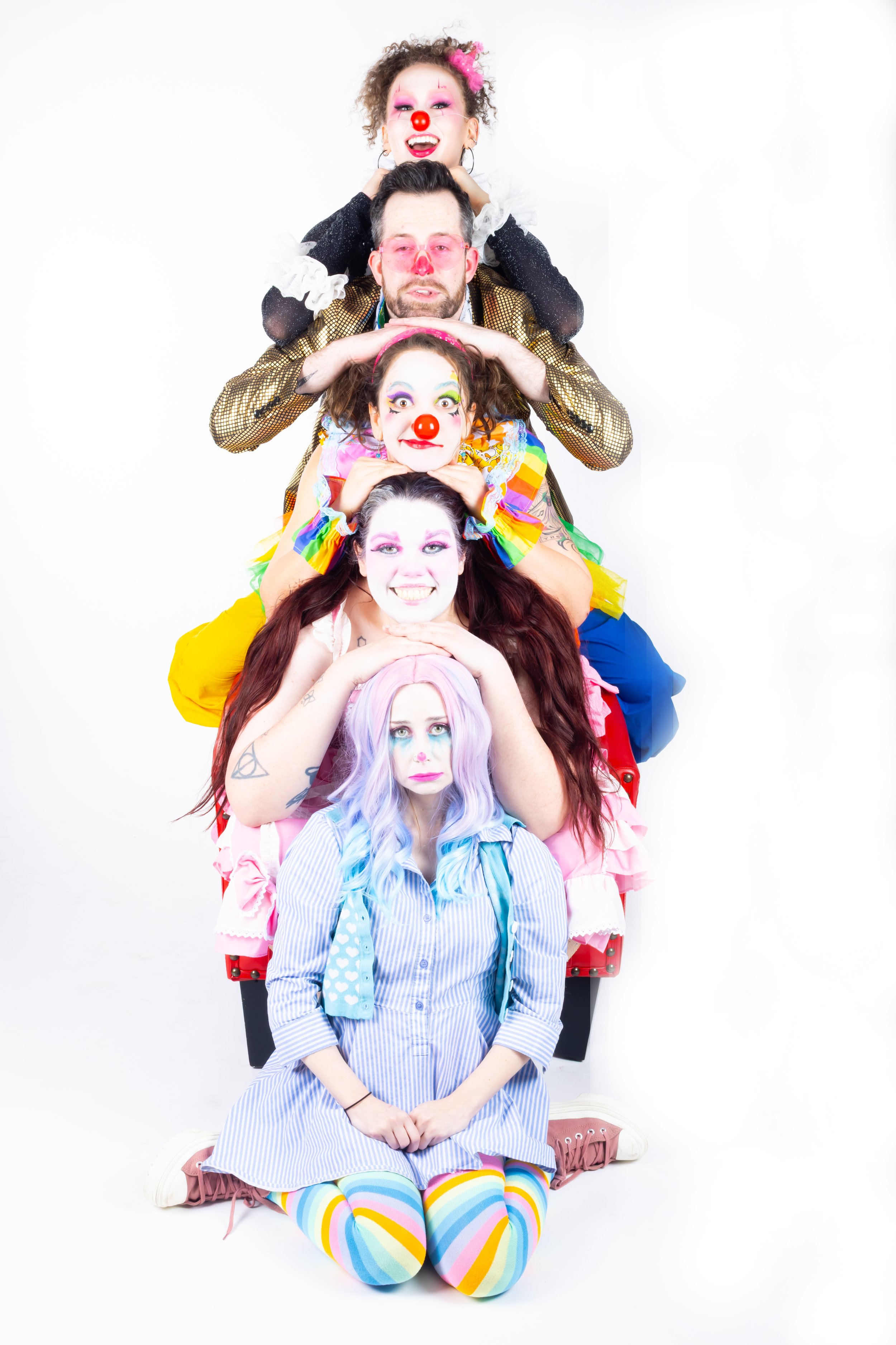 A group of five people dressed as clowns stacked on top of each other in a pyramid form, posing in front of a white background.