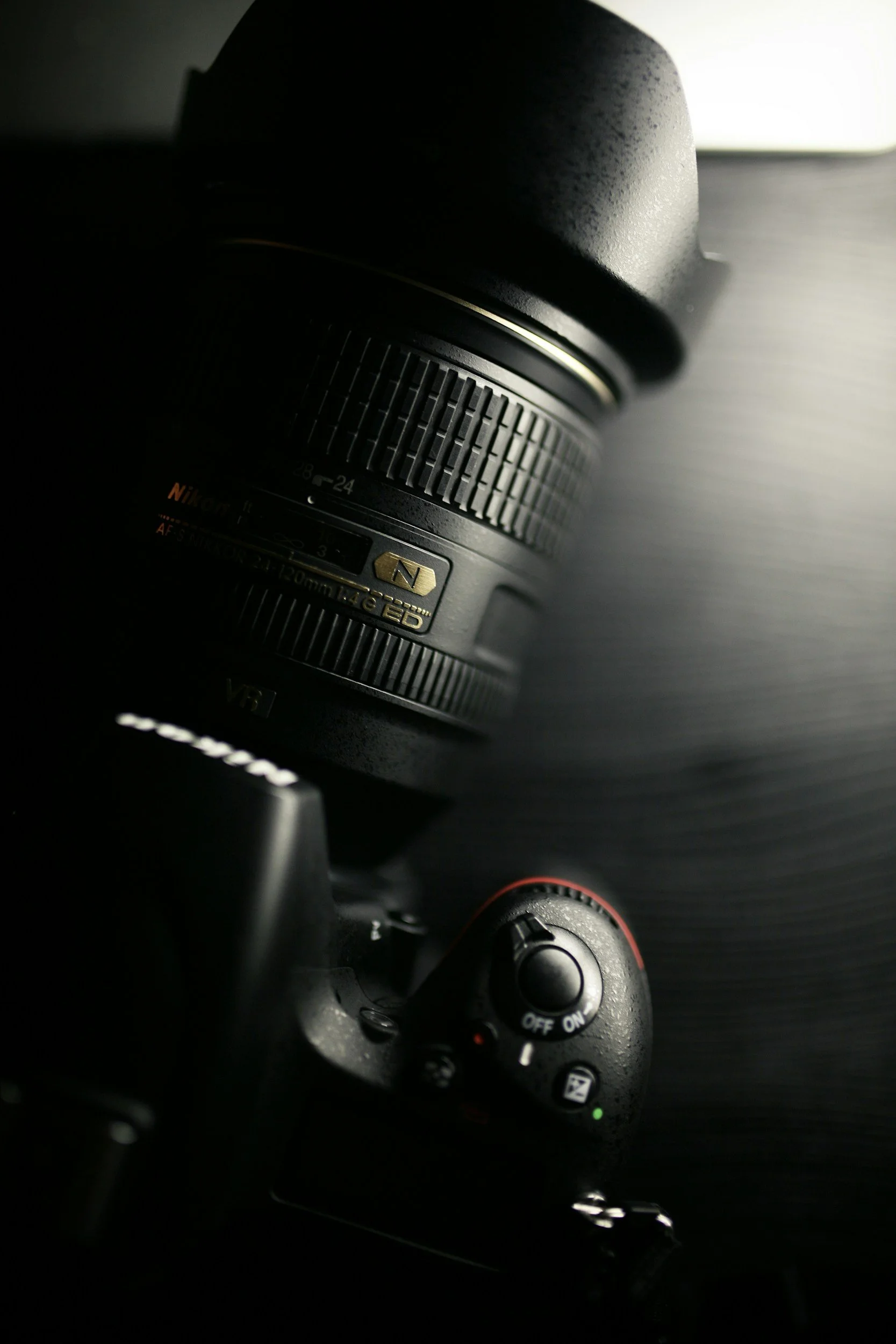 Close-up of a professional DSLR camera with a zoom lens, placed on a dark surface.