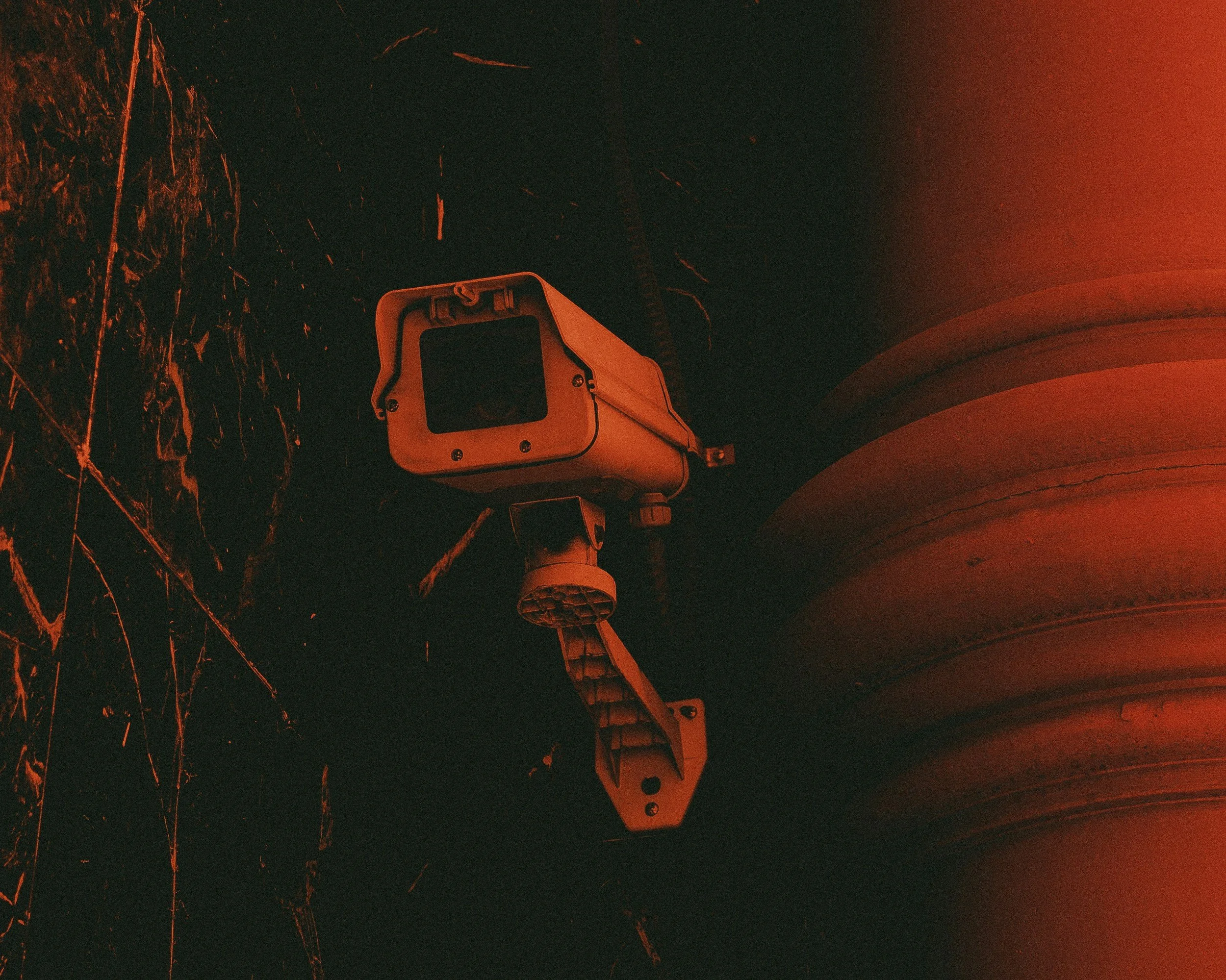 A security camera mounted on a wall with a dark background and red lighting.