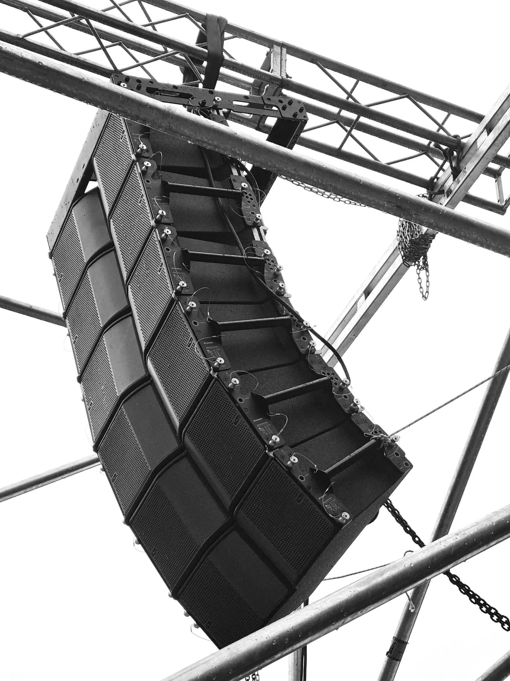 Sistema de altavoces grandes en un escenario, suspendidos en una estructura metálica, en blanco y negro.