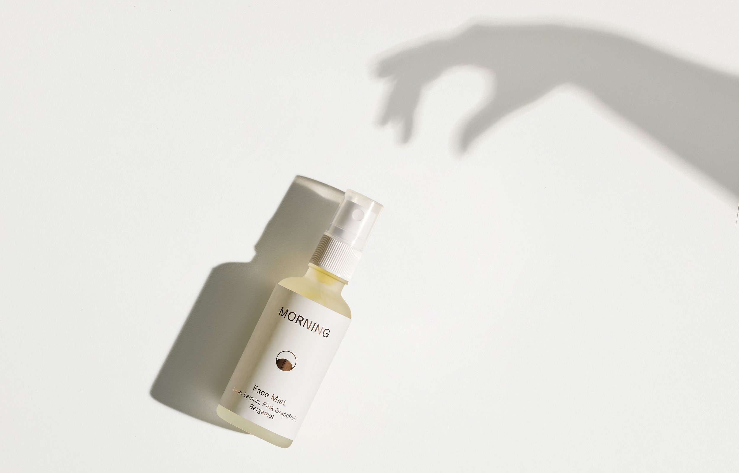 A bottle of morning face mist spray with white label, casting a shadow on a white surface.