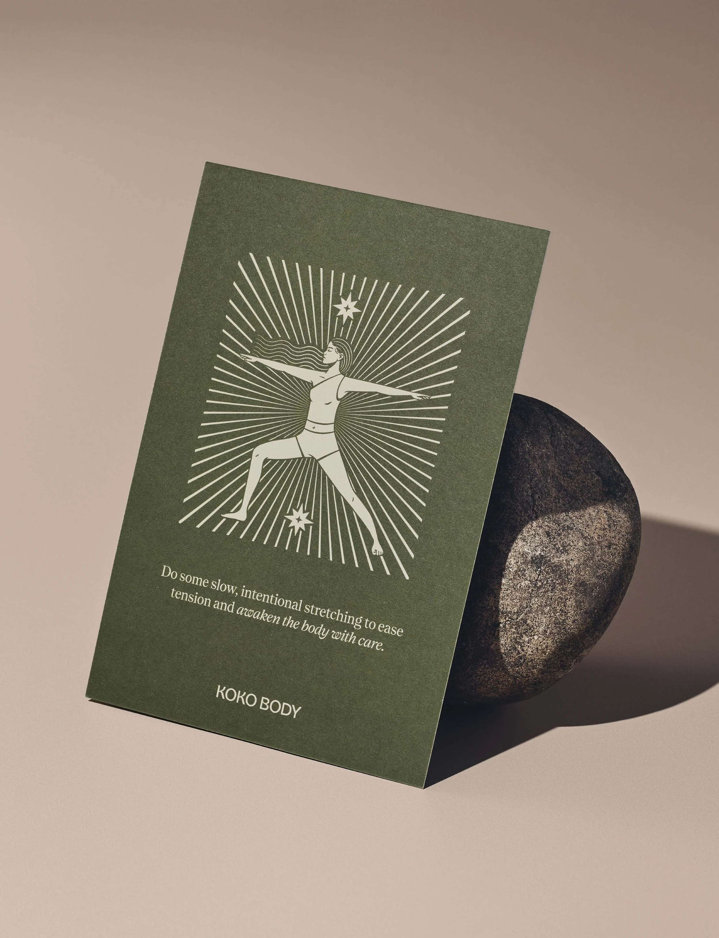 A green card featuring a white line drawing of a woman in a yoga pose with arms outstretched, surrounded by radiating lines and stars. The card has an inspirational message about stretching and awakening the body, and is labeled 'KOKO BODY'.