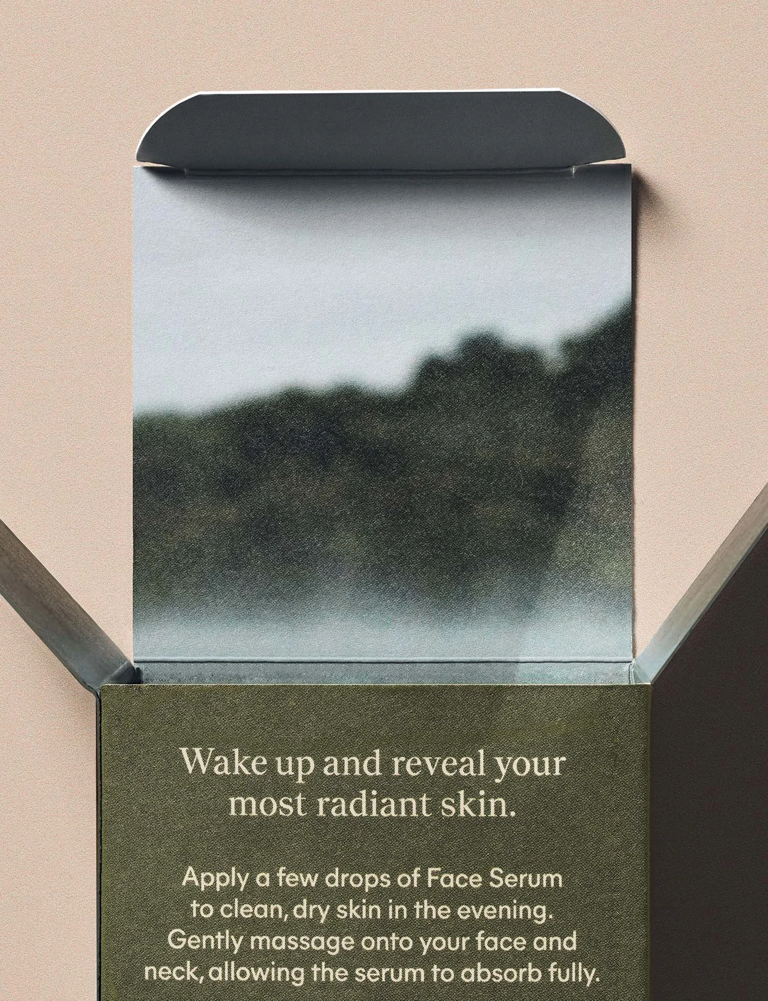 Open skincare box with the lid reflecting a blurry landscape, and instructions on the inner side for applying face serum for radiant skin.