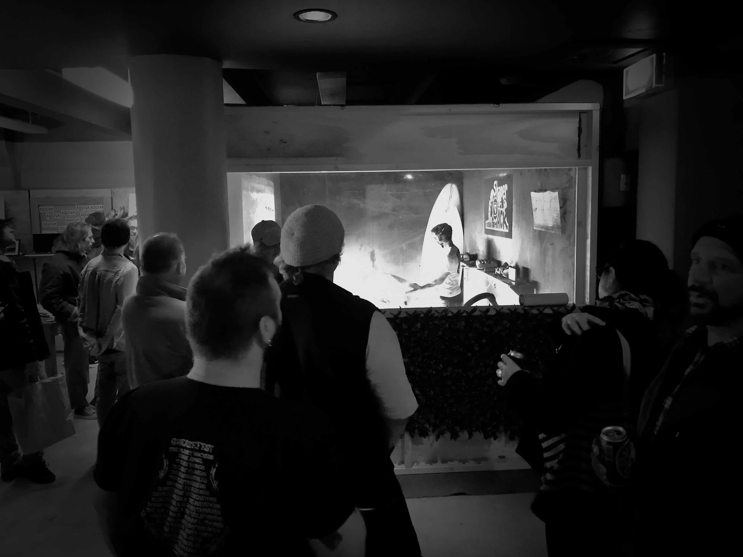 People watching a chef preparing food behind a glass window in a restaurant or food stall.