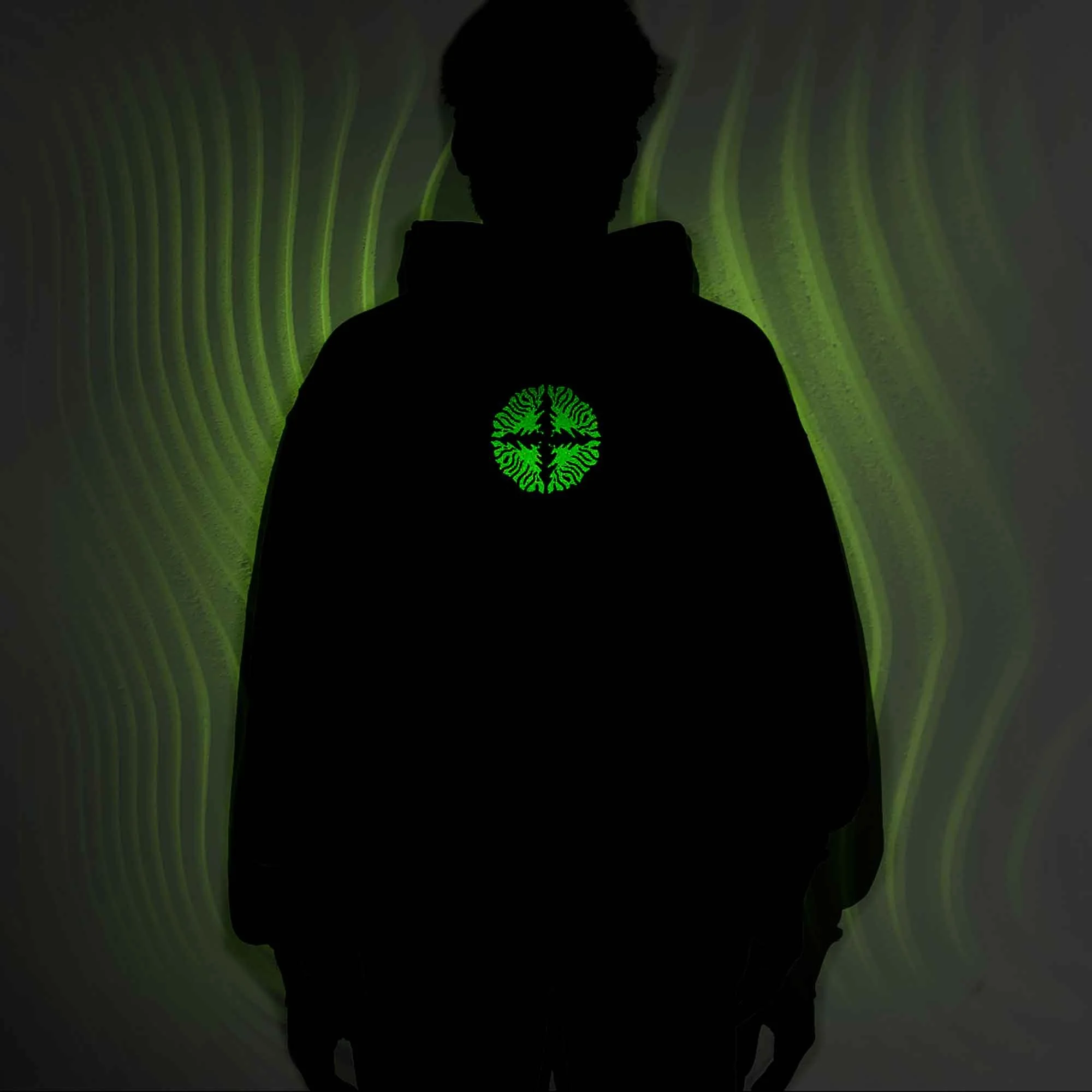 Silhouette of a person wearing a black hoodie with a glowing green logo on the chest, standing in front of a green patterned background.