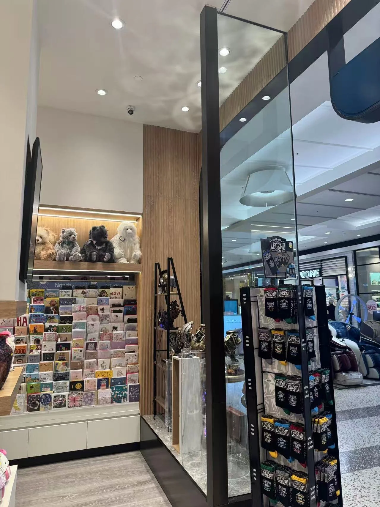 Inside a shopping mall, featuring a display of greeting cards and plush teddy bears.