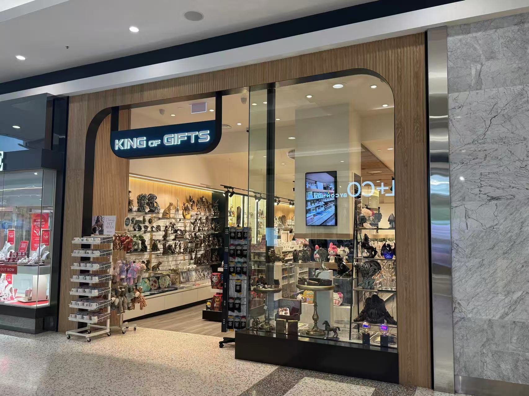 Storefront of KING of GIFTS selling decorative items, plush toys, and accessories displayed on shelves and tables inside a mall.