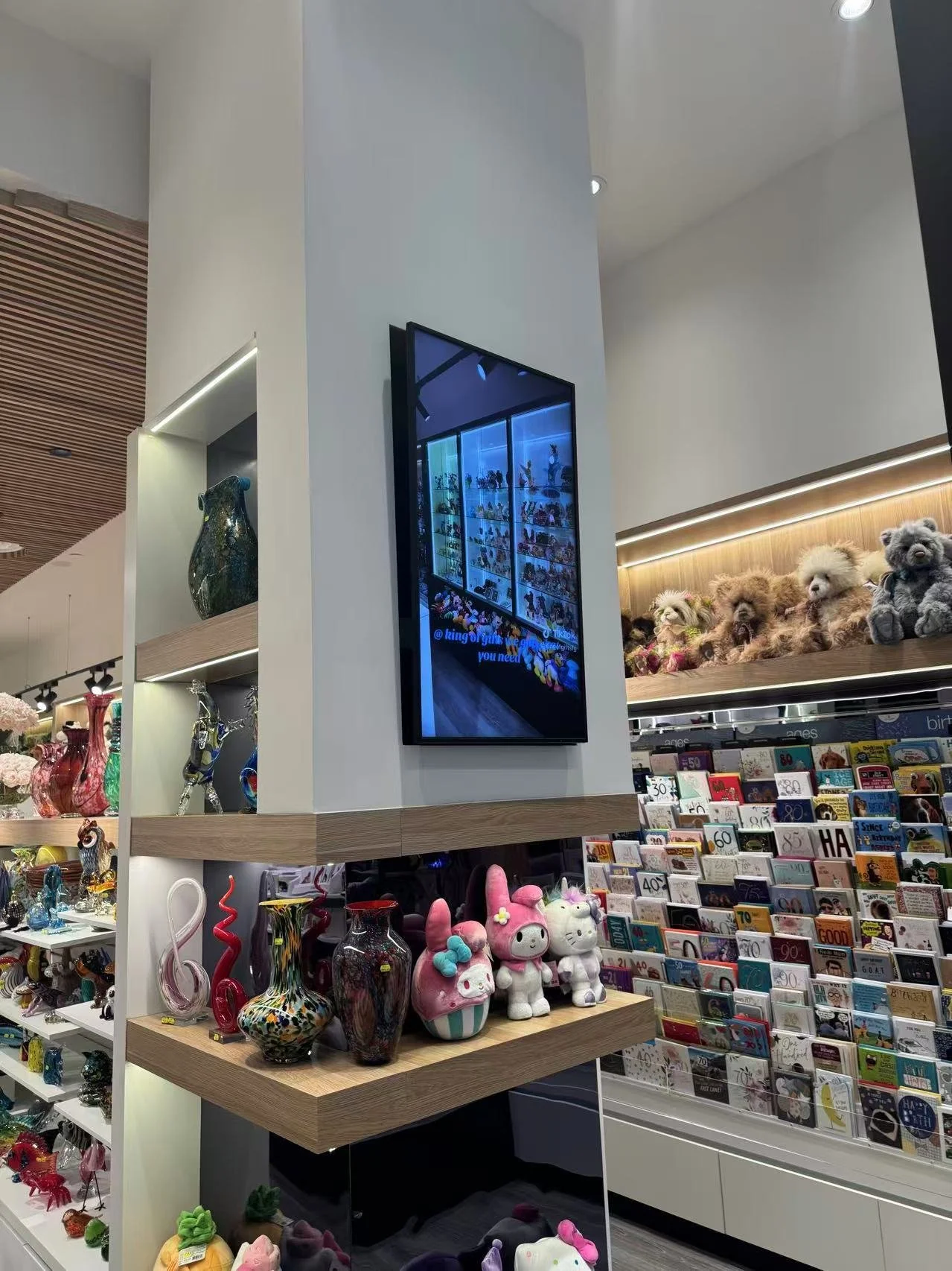 Display of colorful glass vases, plush toys, and greeting cards on shelves in a store.