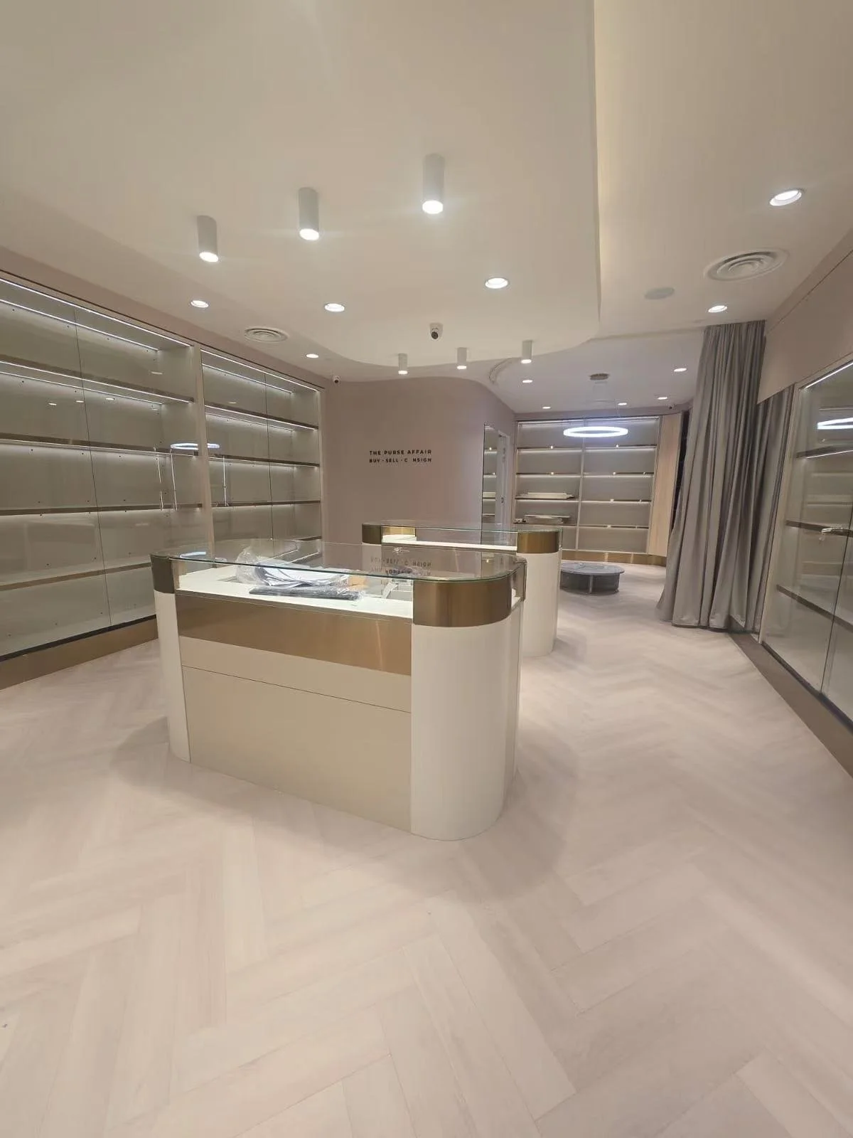 Empty retail store with glass display counters, shelving units, and a circular light fixture on the ceiling.