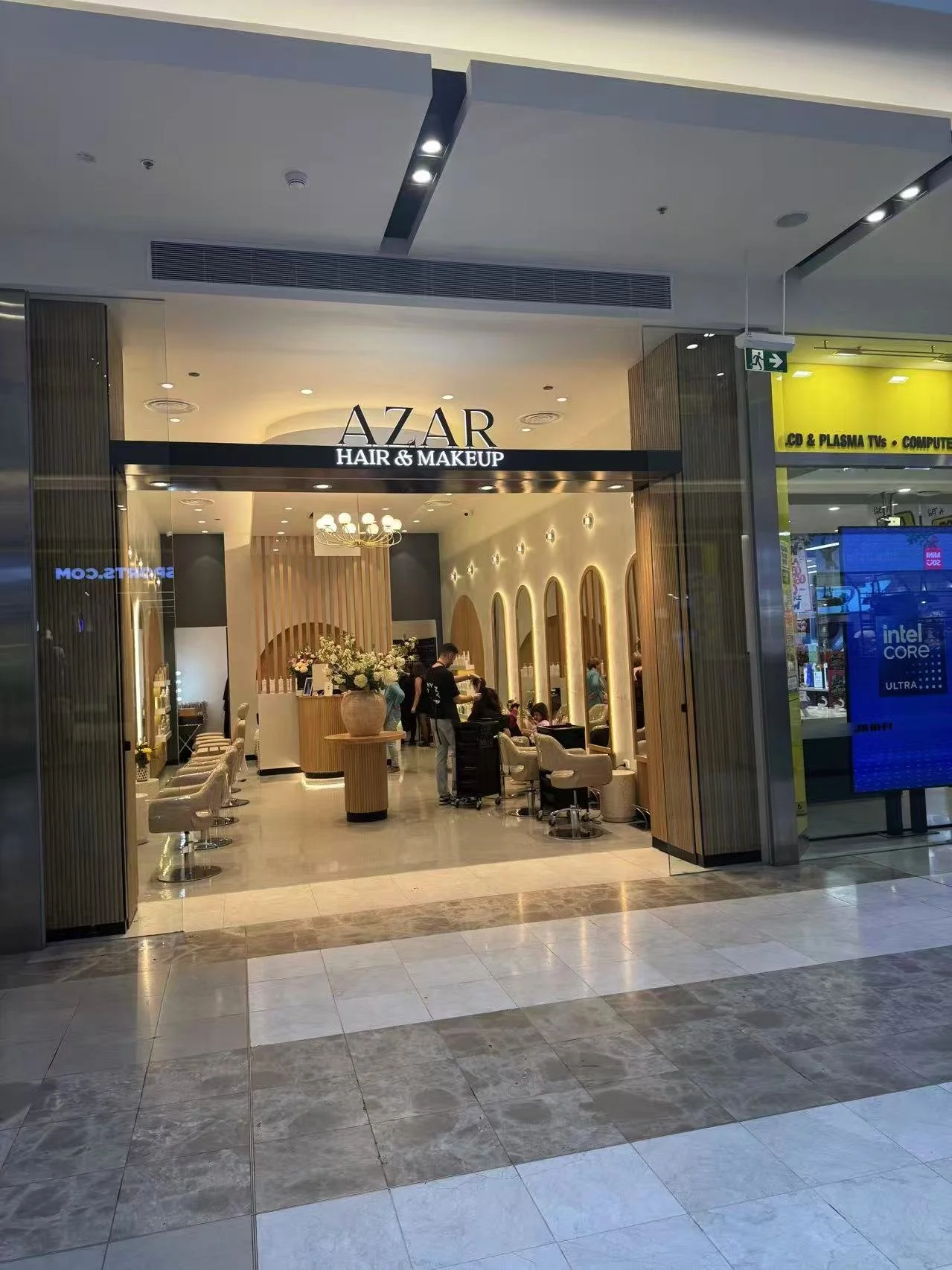 Entrance to a hair and makeup salon named AZAR inside a shopping mall with seating area and decorative interior design.
