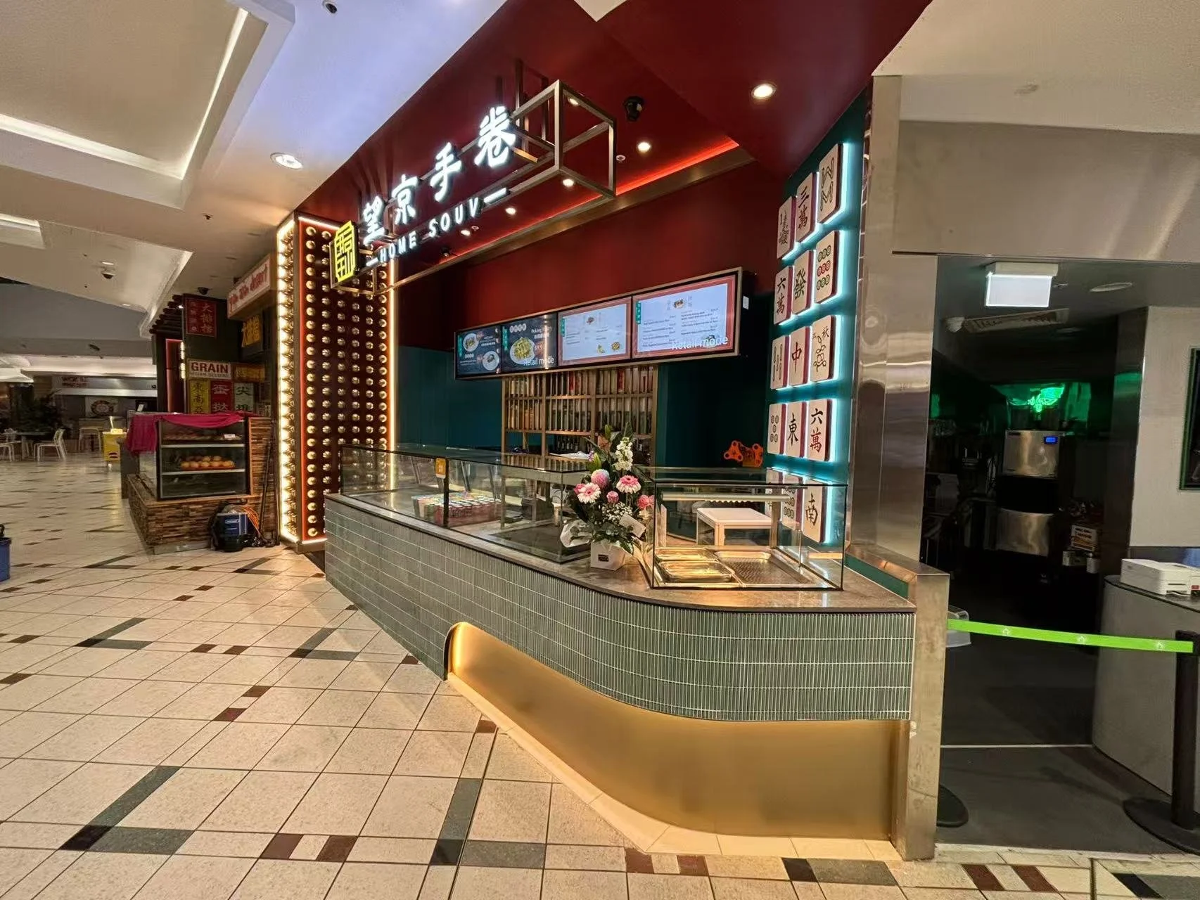 Food counter at a restaurant named 'Home Souv' with digital menu screens, decorative tiles, and a flower arrangement on the counter.