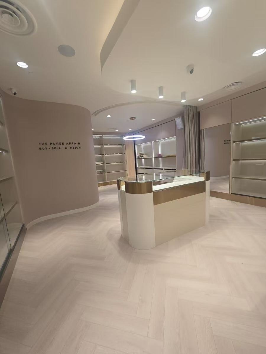 Empty retail store with beige and white decor, display shelves, and a central glass-topped counter.