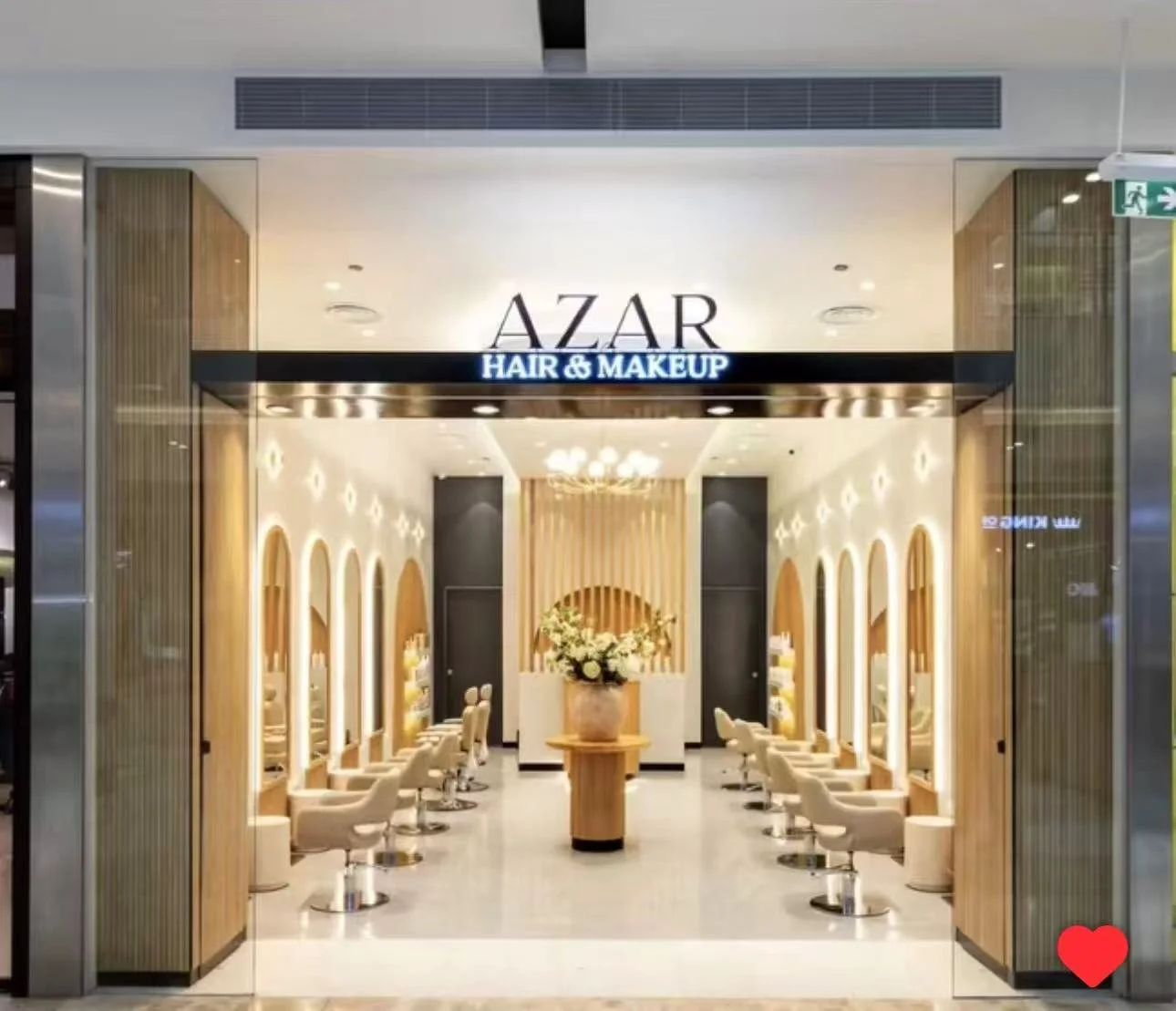 Entrance to Azar Hair & Makeup salon with beige chairs, a central flower arrangement, and modern interior decor