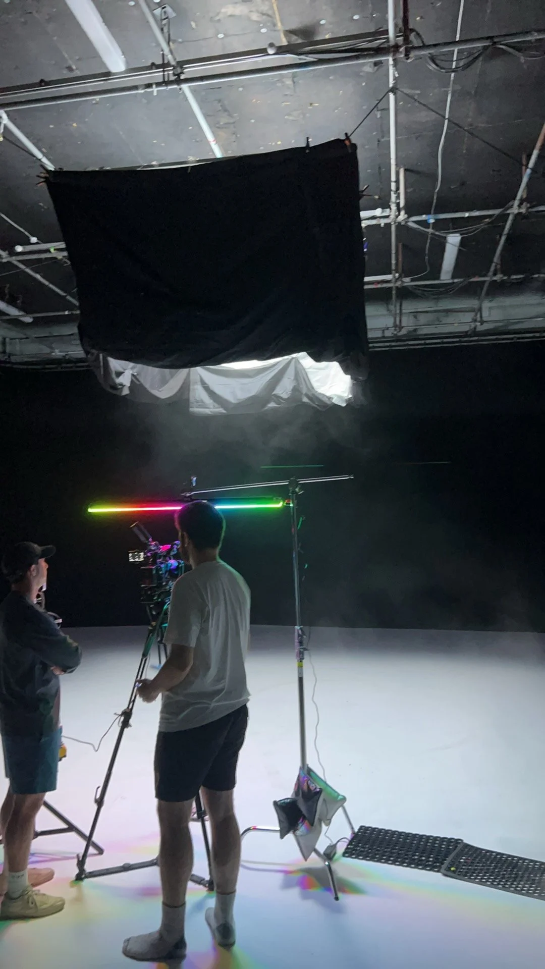 People working on a film or photography shoot in a studio with black background and studio equipment, including a multicolored light.