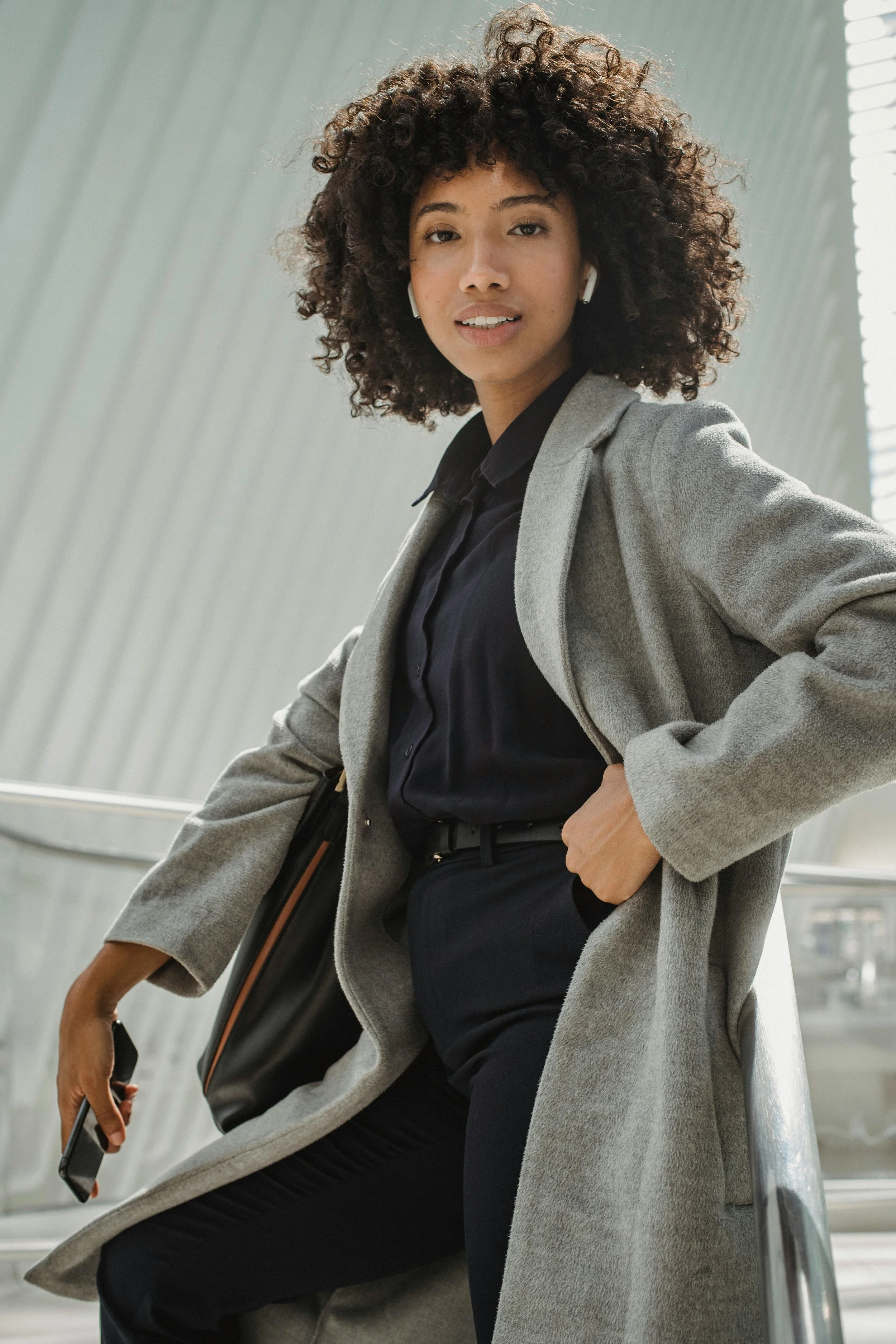 A woman in professional attire seated alone at a boardroom table, hands clasped, direct eye contact — composed, certain, and fully present.