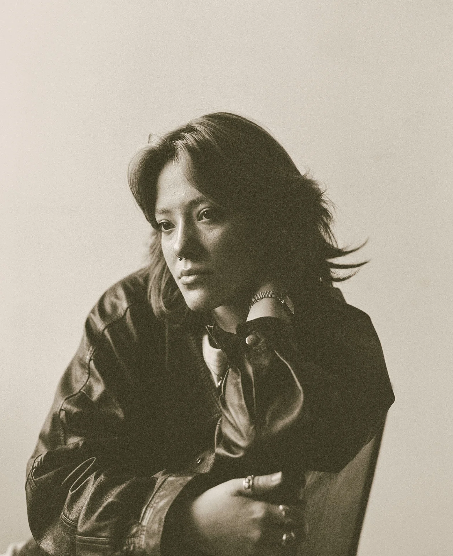 A black and white portrait of a young woman with shoulder-length hair, wearing a leather jacket and a choker, looking slightly to the side.