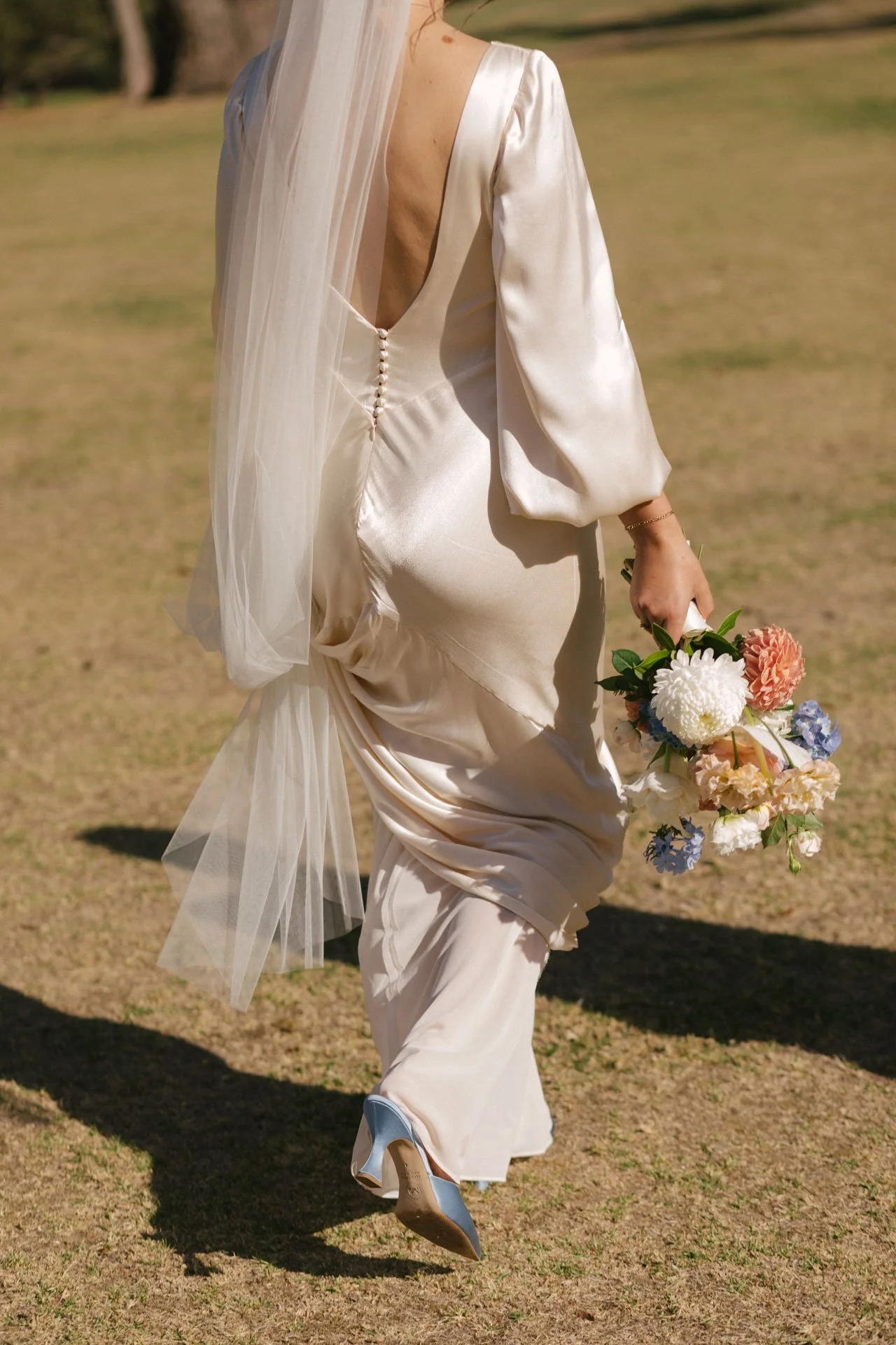 A woman in a satin wedding dress holding a bouquet of flowers in an outdoor setting.