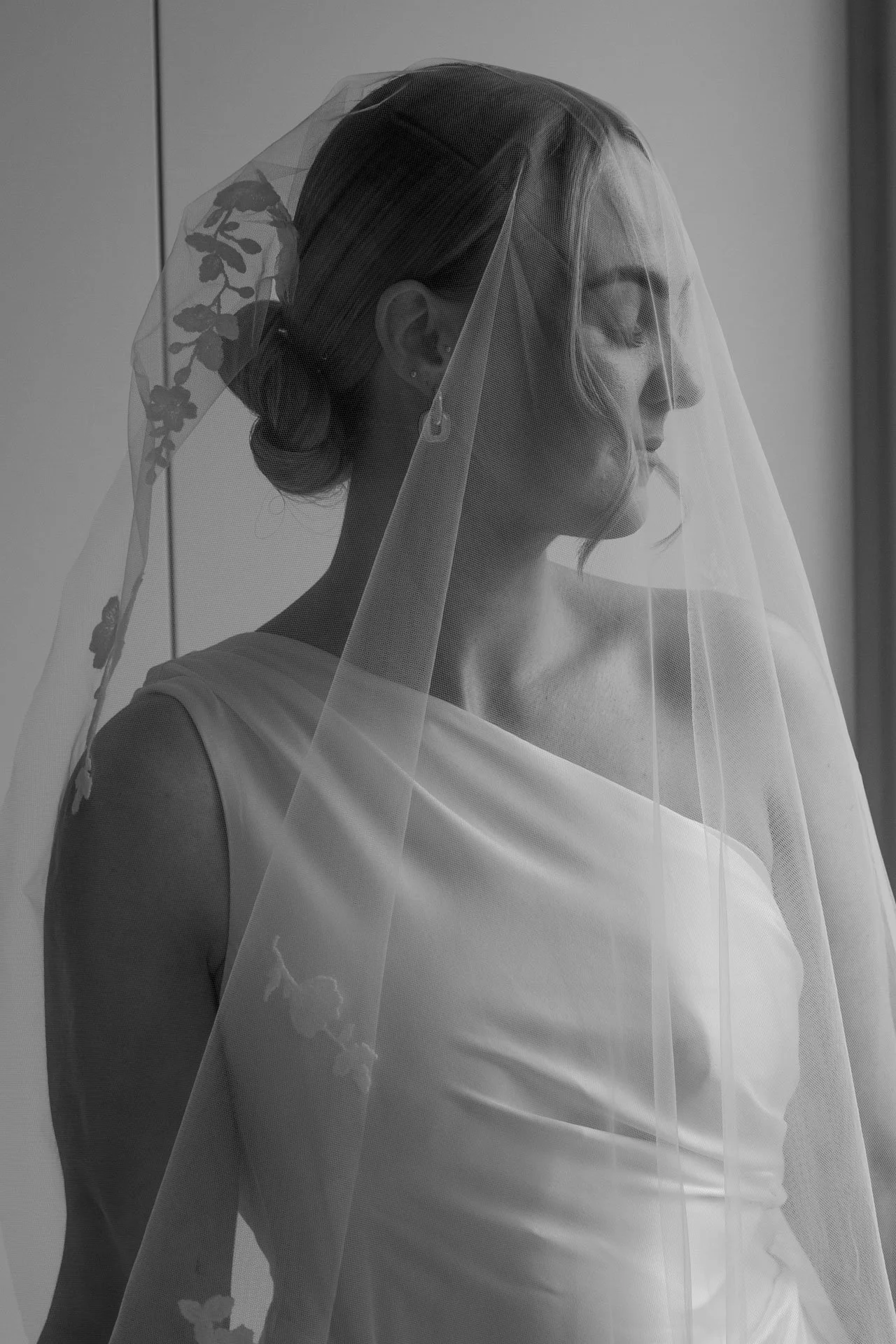 Black and white photo of a woman wearing a wedding dress and veil, smiling with her eyes closed.