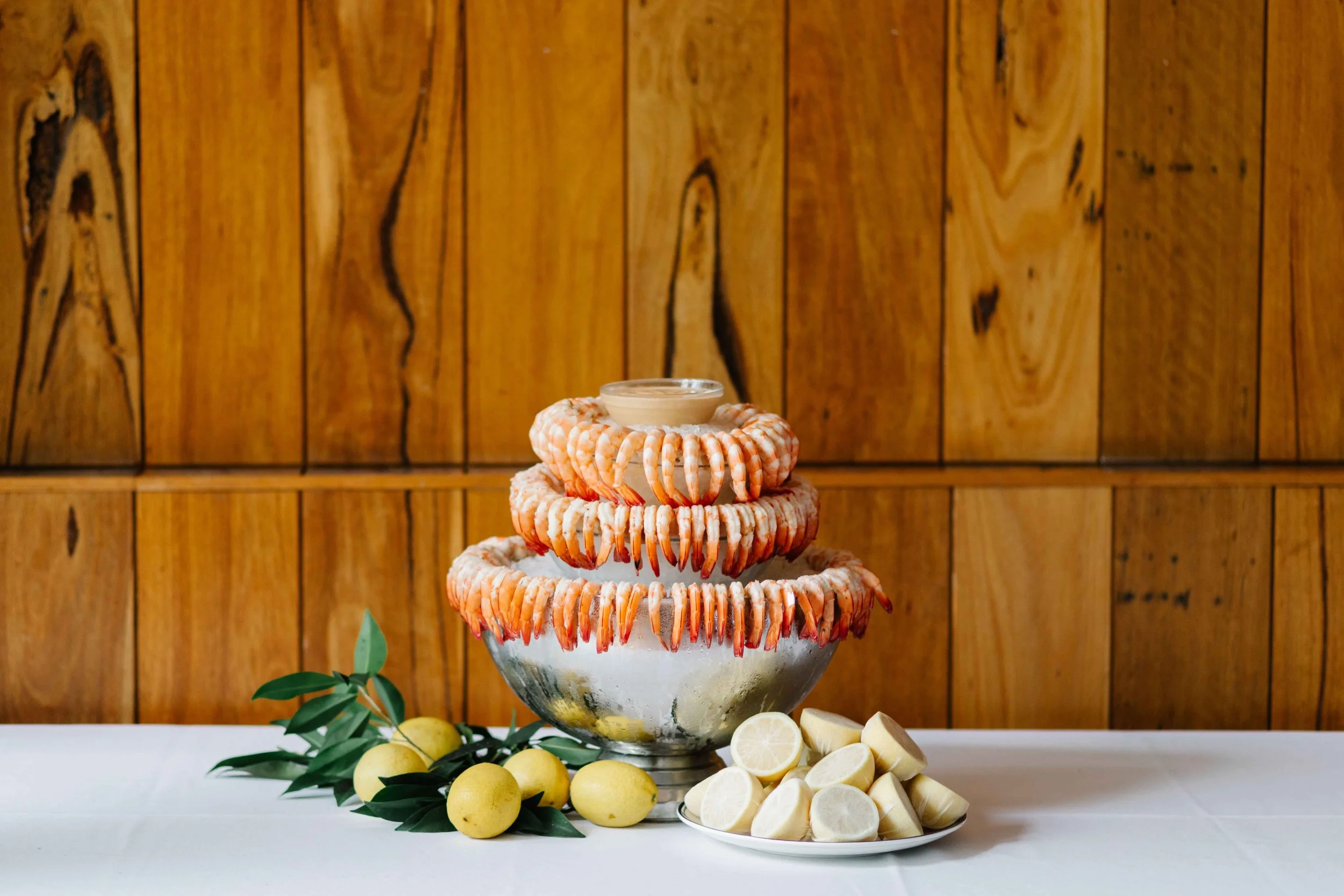 Tiered dessert stand with lemon and lemon slices, garnished with green leaves, set against a wood-paneled background.