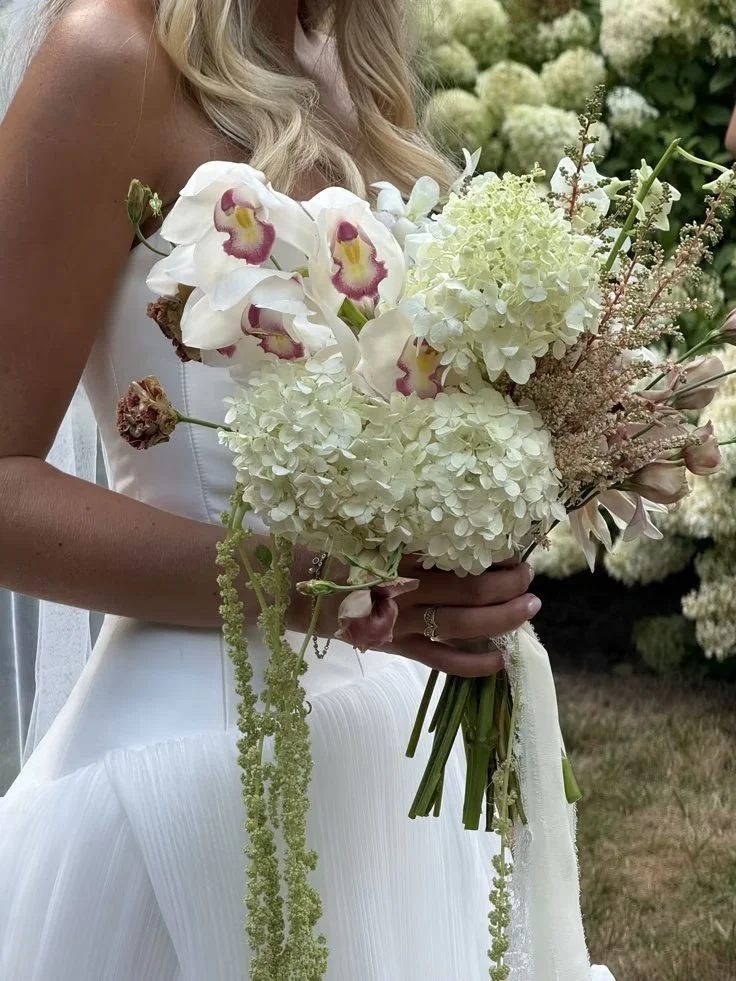 A bride wearing a white strapless wedding dress holding a bouquet of white and pink orchids, hydrangeas, and other flowers.
