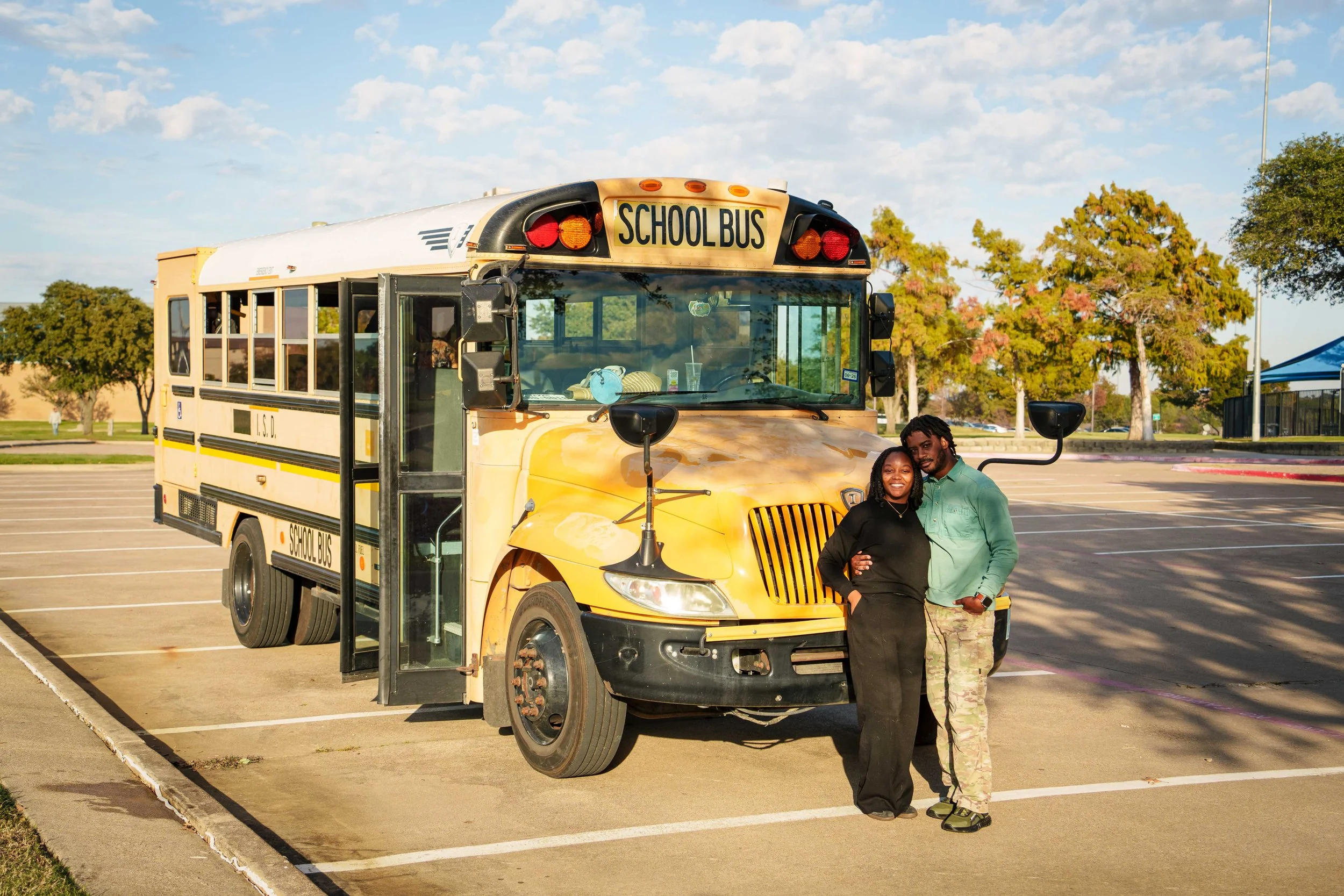 Two people standing in front of a school bus in a parking lot, smiling and posing for the photo.