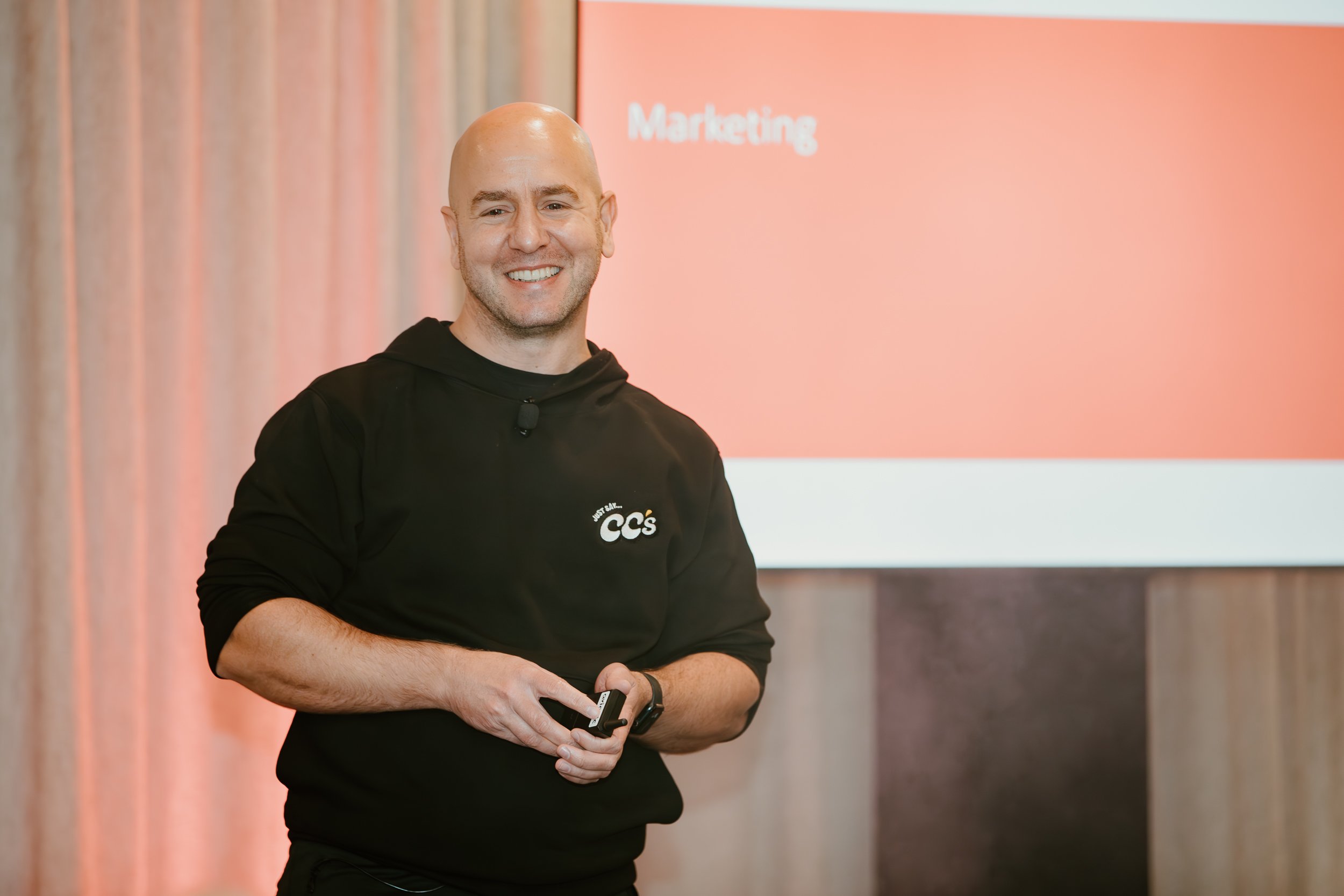 James Deysel doing a public speaking event about Marketing. James Deysel is dressed in a hoodie and is on stage, smiling.