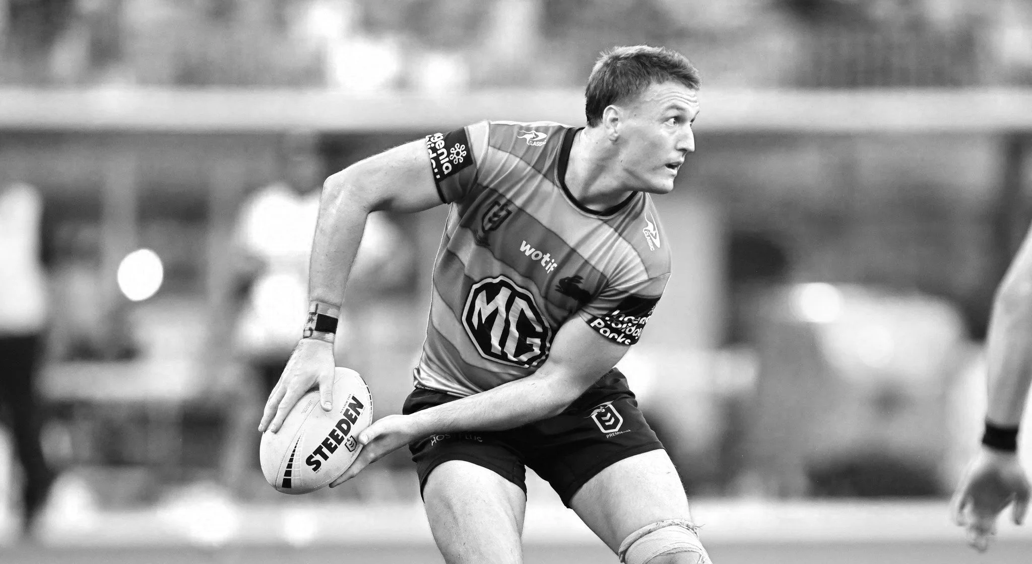 A male rugby player in a striped jersey holding a rugby ball during a game, with a blurred background.