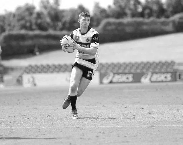 A male rugby player holding a rugby ball on a field, preparing to run, in black and white.
