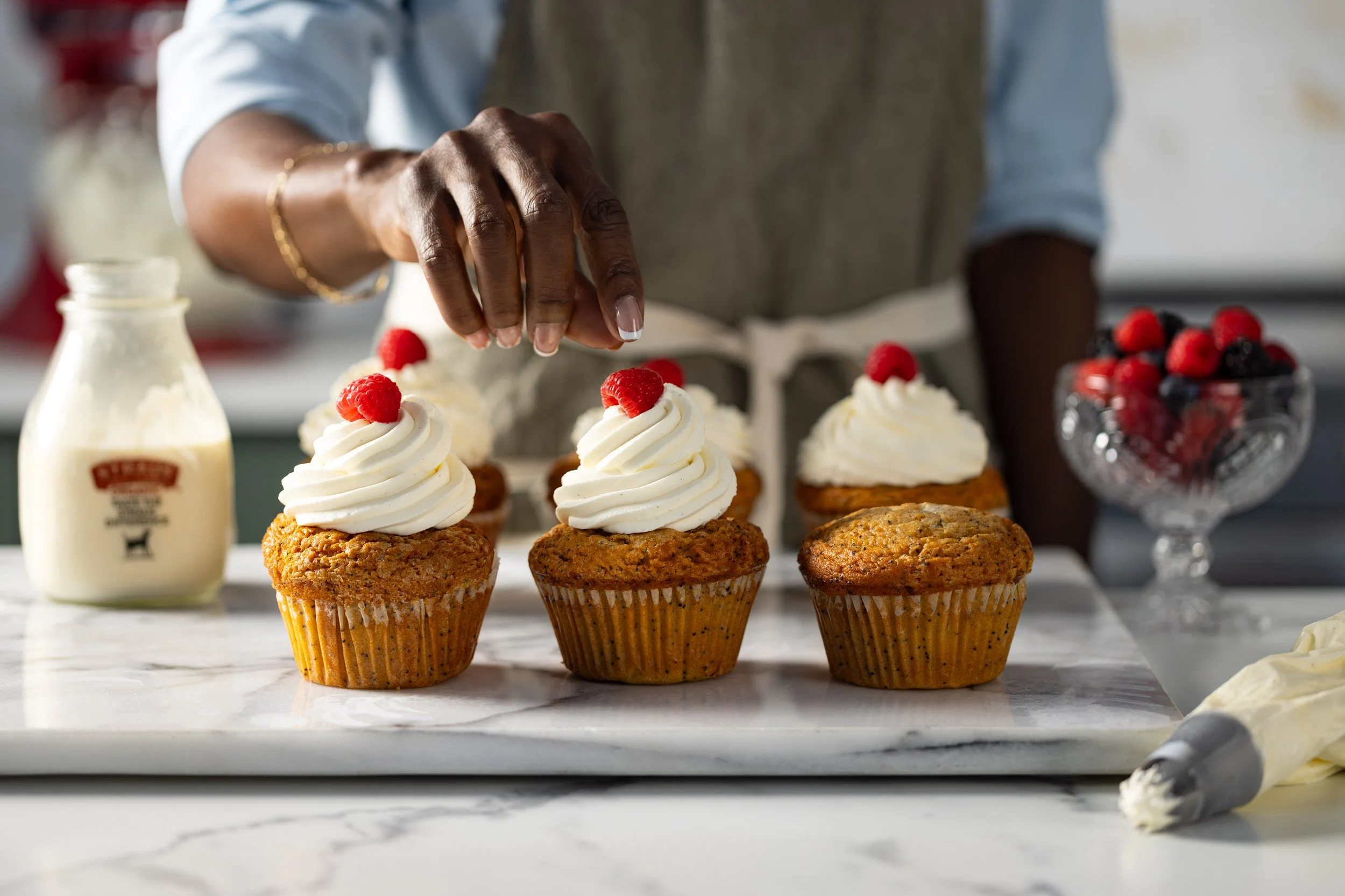 Lifestyle food photograph showing a woman decorating some cupcakes.