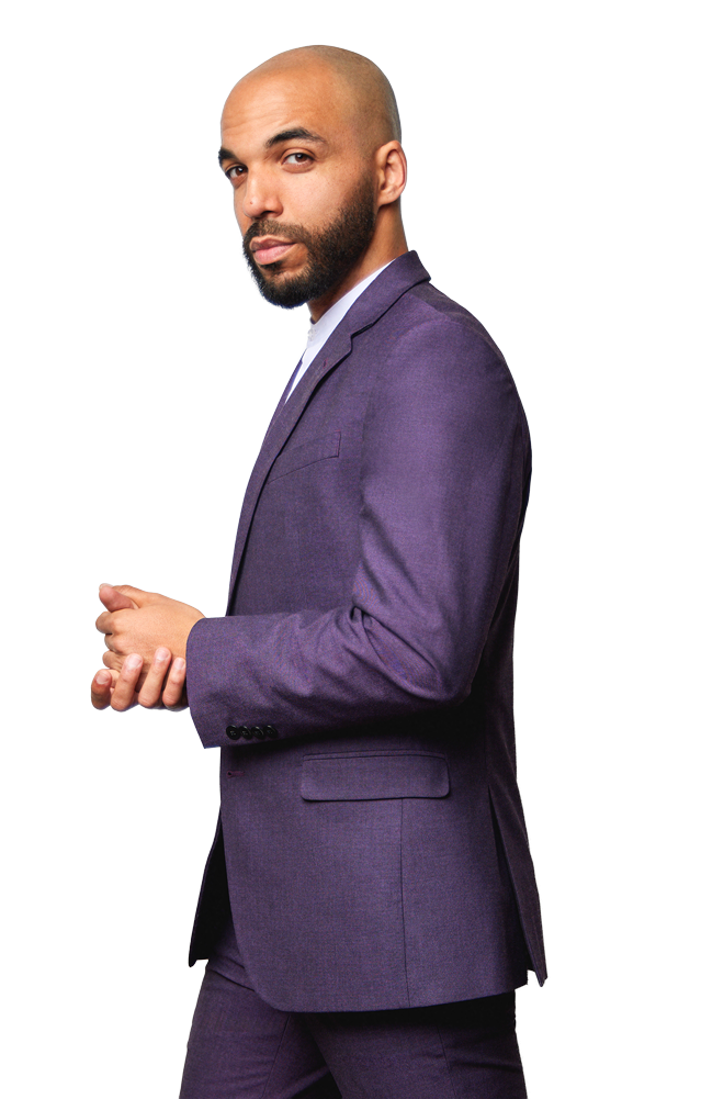 A man with a shaved head and beard wearing a purple suit with a white shirt, standing against a white background.