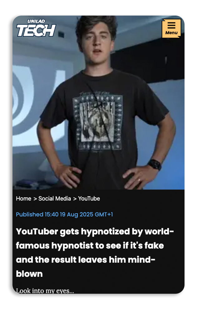 A young man with dark, curly hair stands with hands on hips in front of a presentation screen, wearing a black T-shirt with a graphic print, in a modern tech or educational setting.