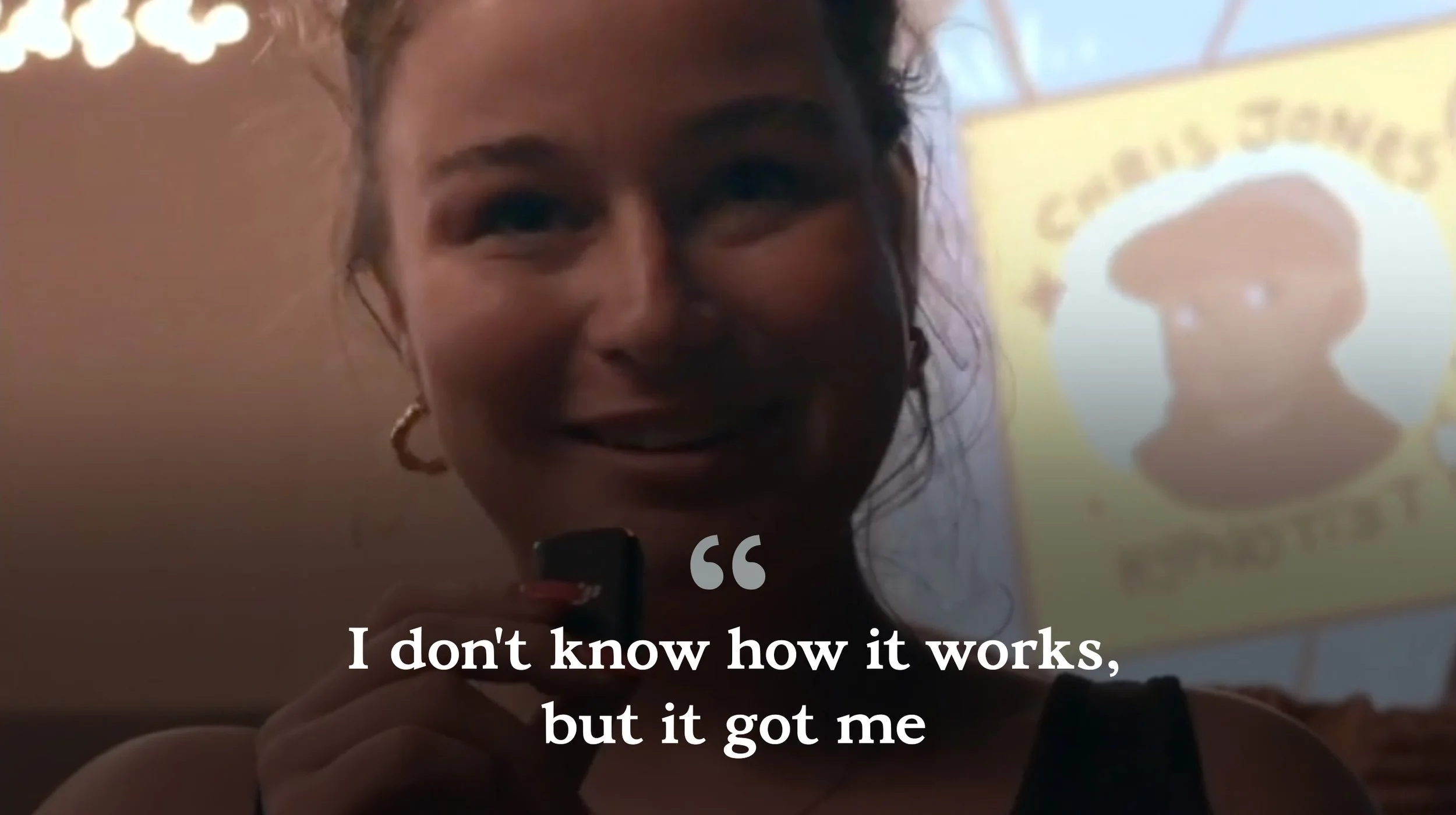 A woman smiling while holding a microphone in front of a projection screen that displays an emoji with sunglasses and the phrase "I don't know how it works, but it got me."