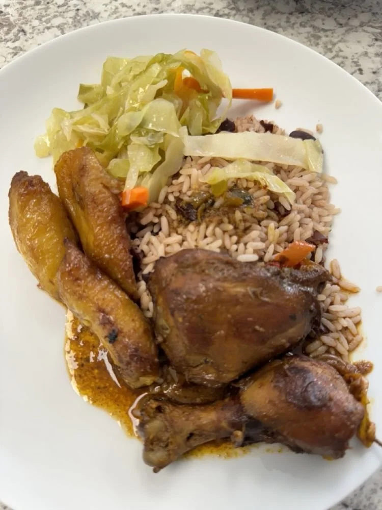 Plate of cooked rice with vegetables, fried plantains, and chicken drumsticks.