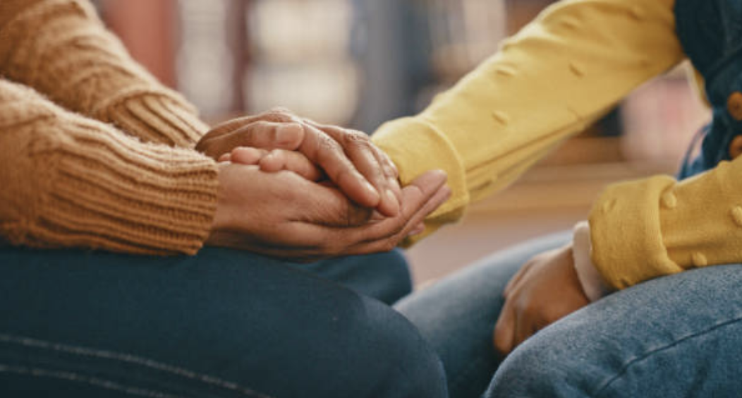 Two people holding hands, one person with darker skin in a Plymouth sweater, the other with lighter skin wearing a yellow sweater.
