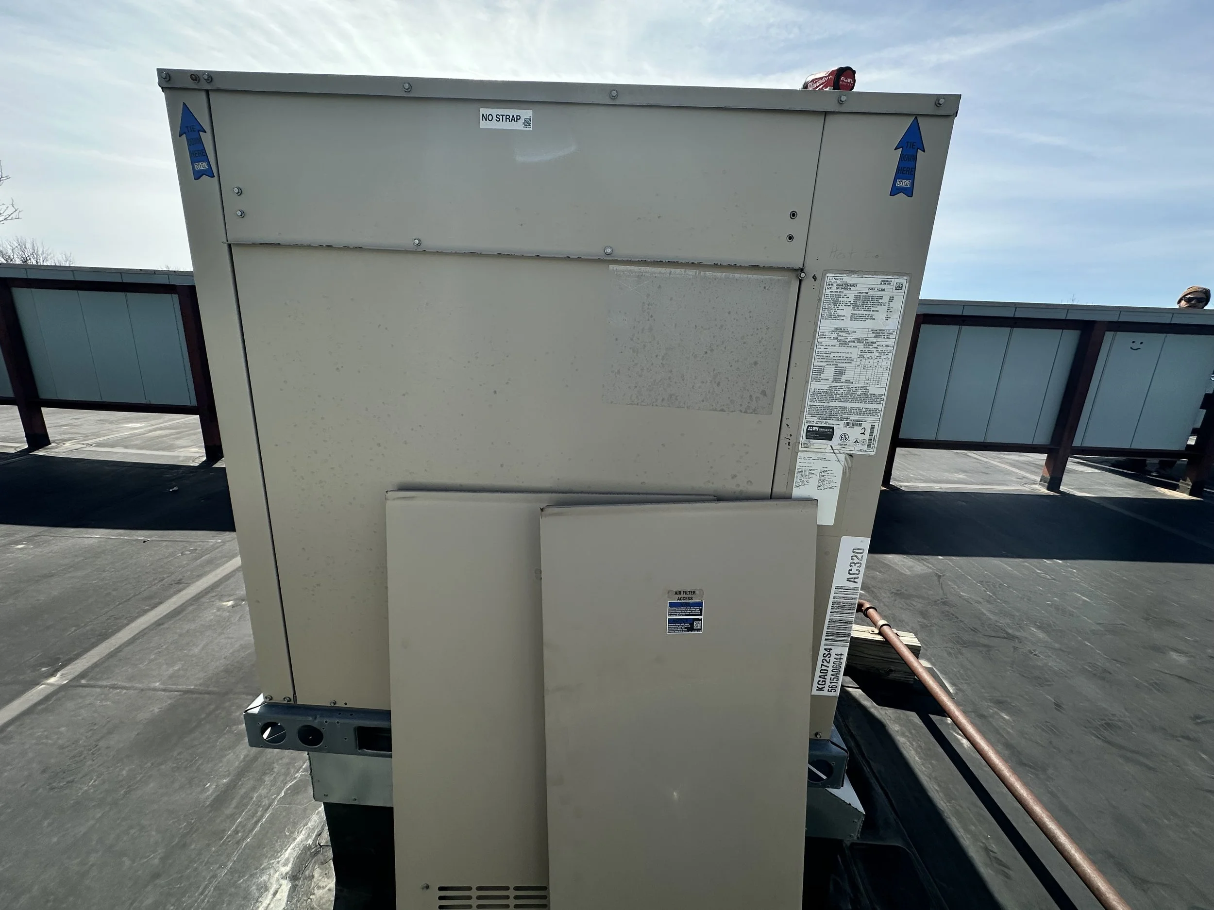 Back view of a large HVAC rooftop unit on a flat roof, with a blue sky background.