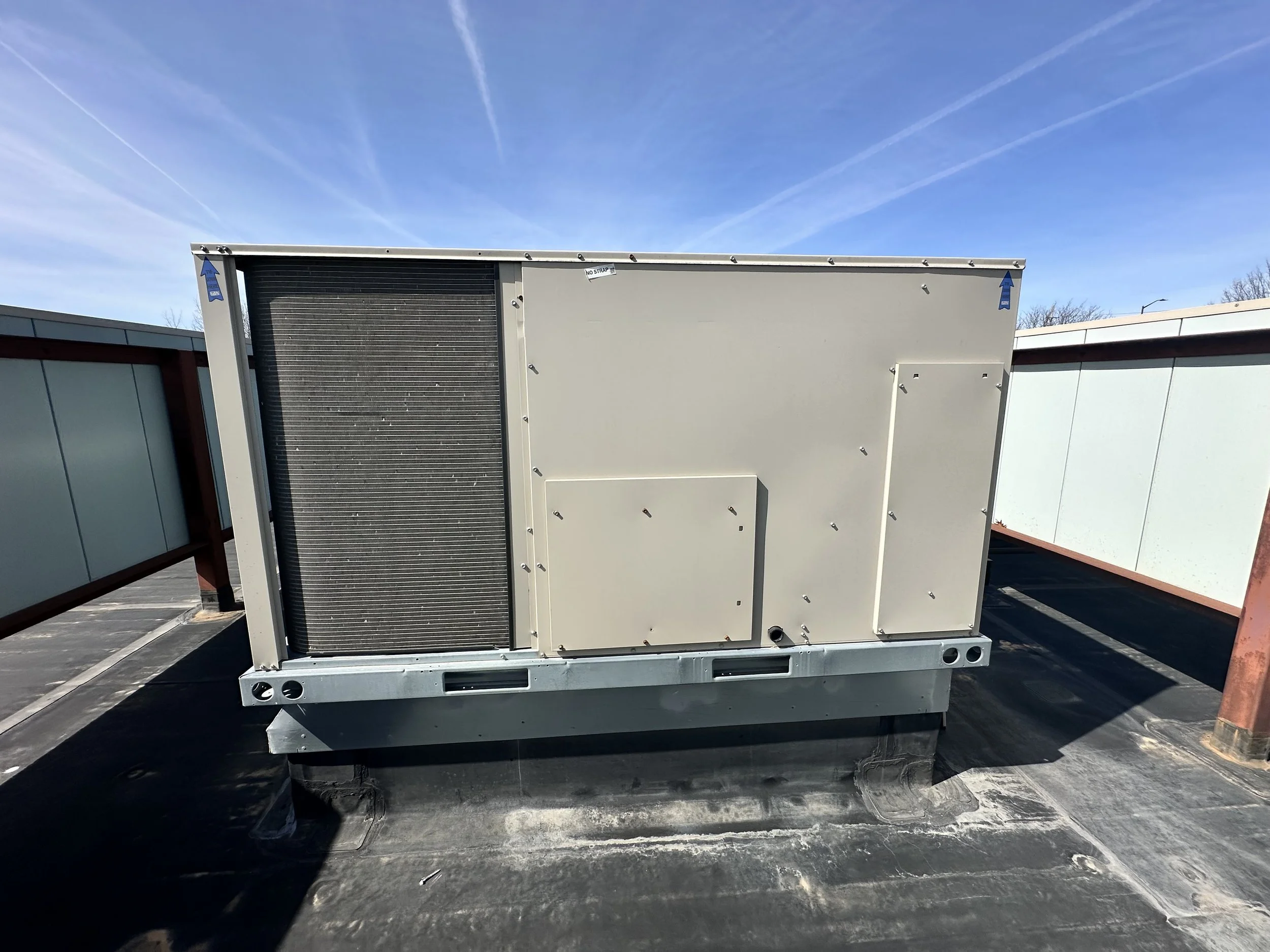 Air conditioning unit installed on a rooftop with blue sky and contrails in the background.