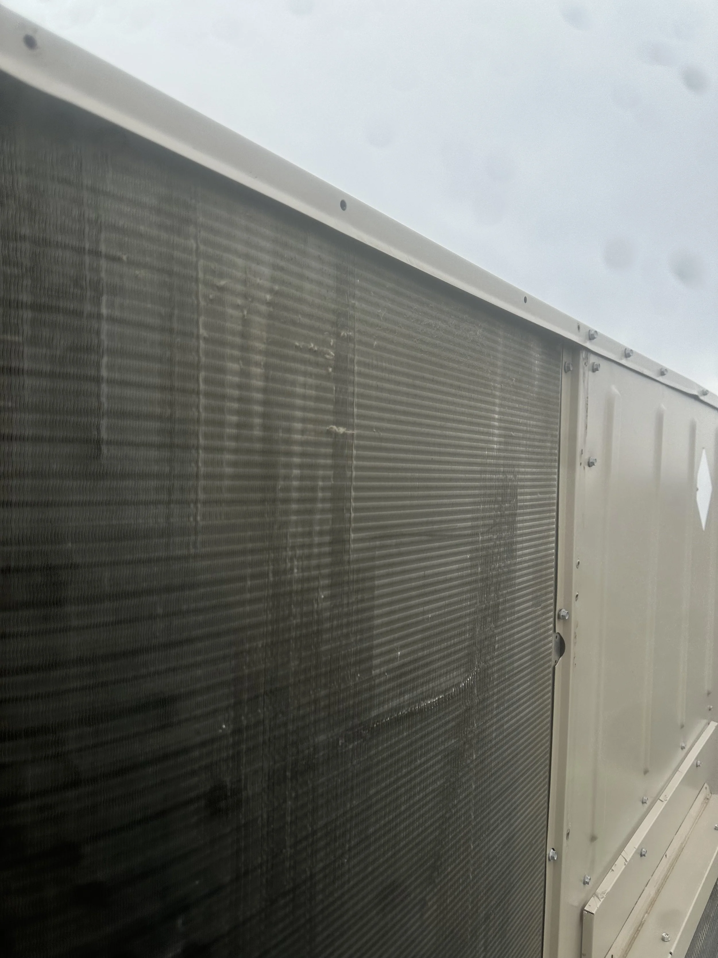 Close-up of the side of an aircraft or industrial vehicle with a metallic, ribbed surface and a white frame, with an overcast sky in the background.