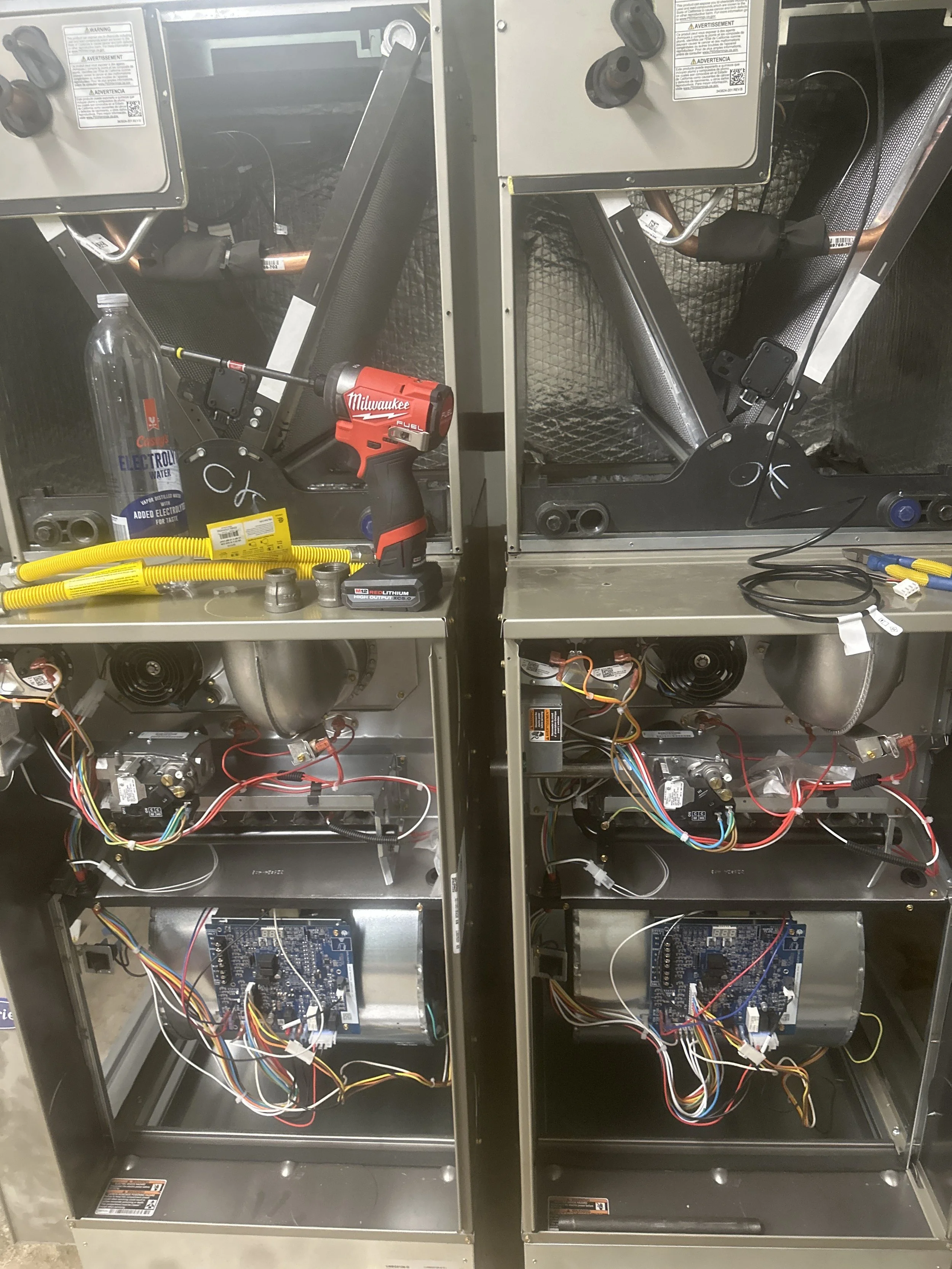 Two HVAC units with open panels showing internal components, wiring, and motors, with tools and items placed on top.