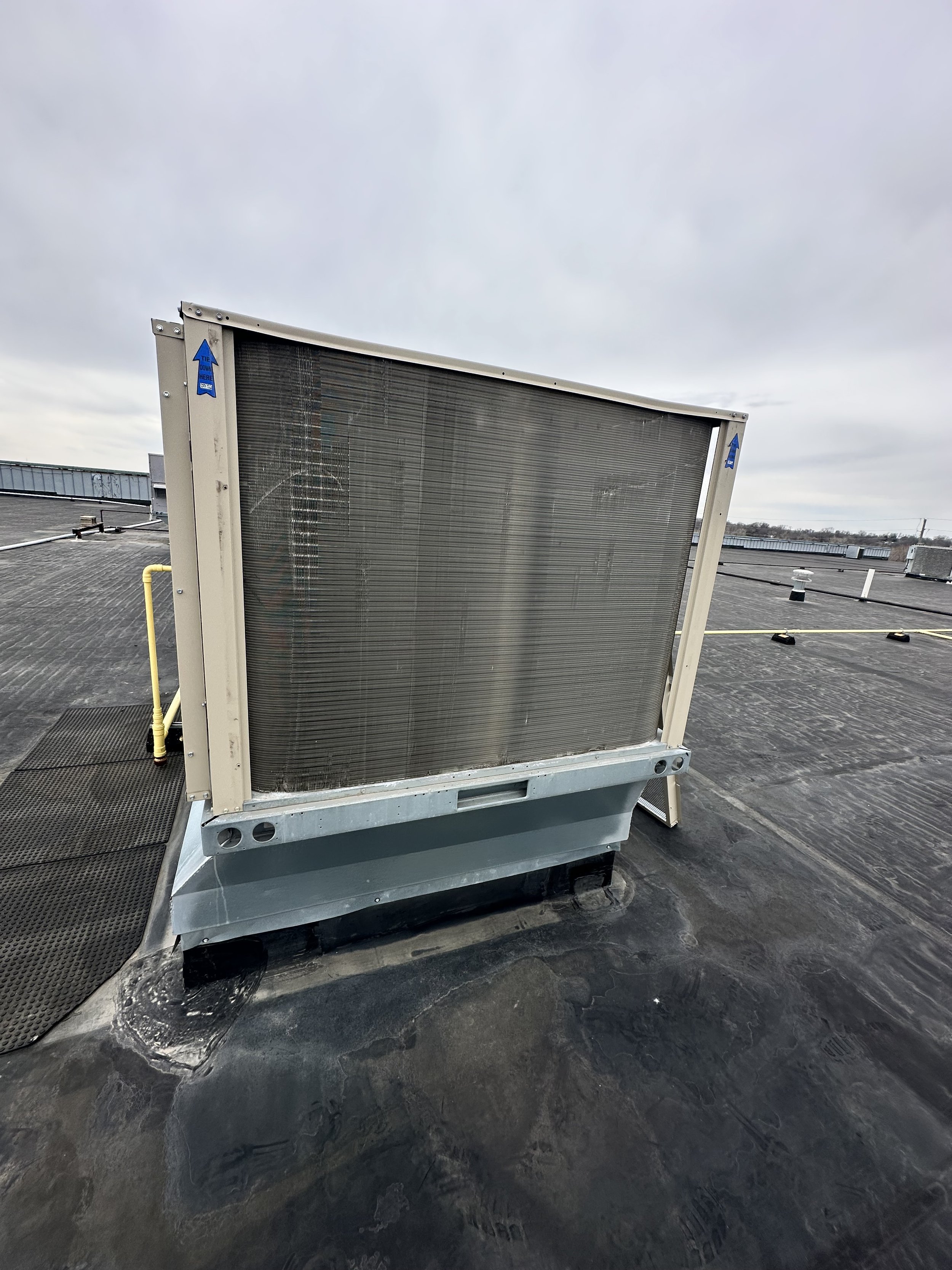 A rooftop air conditioning unit on a flat black roof against a cloudy sky.