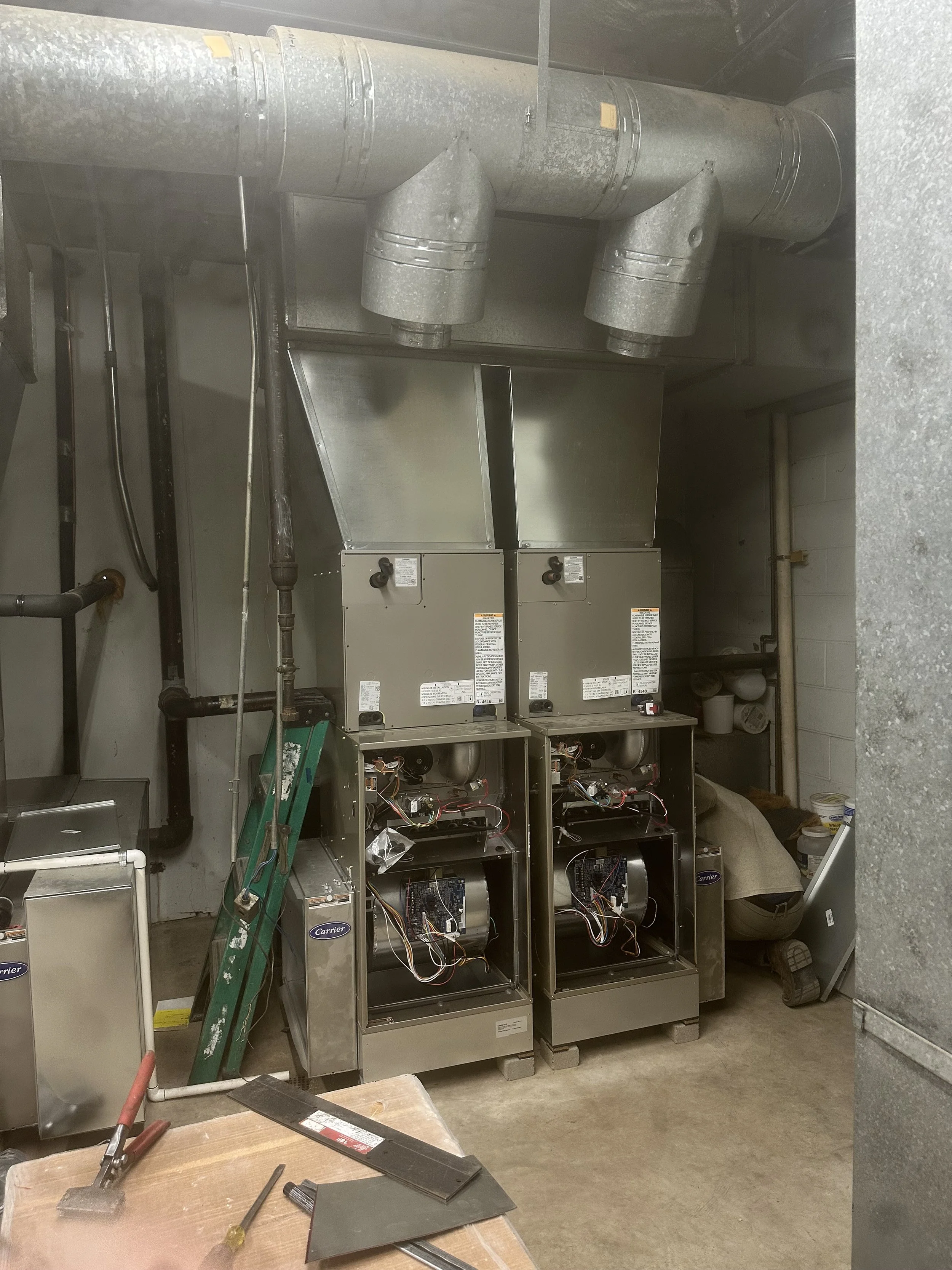 Two disassembled HVAC units with exposed wiring in a utility room.