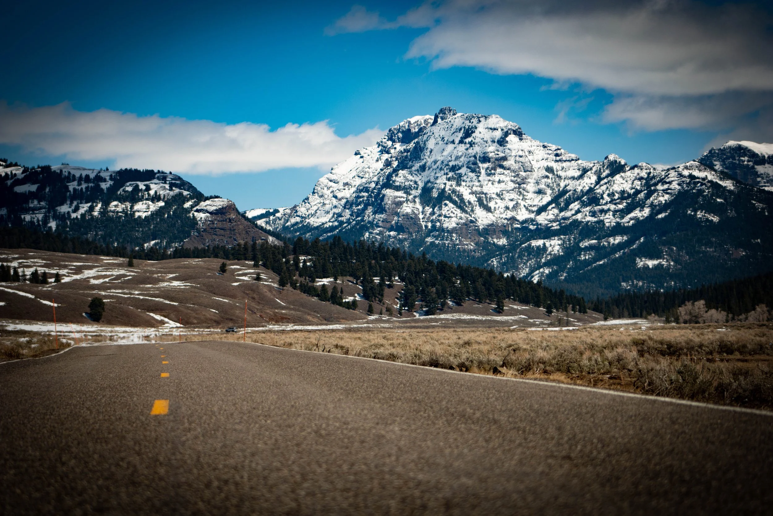 Scenic view of a road leading towards snow-capped mountains under a partly cloudy sky.