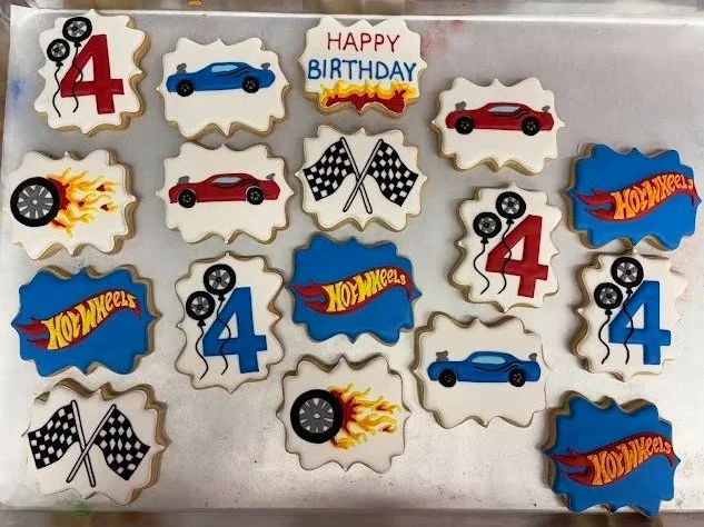 Collection of decorated cookies with racing car themes, number 4, flaming tire, checkered flags, and 'Happy Birthday' message.