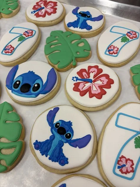 Cookies decorated with Disney's Stitch characters, tropical flowers, and green leaves.