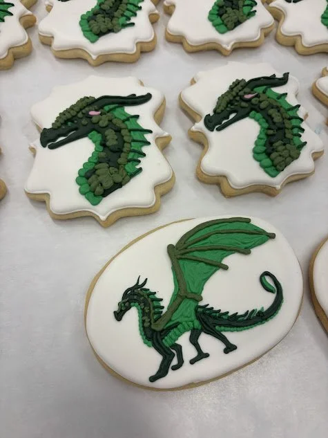 Cookies decorated with green and black dragon designs, including an oval cookie with a detailed dragon illustration and other cookies with simplified dragon head images.