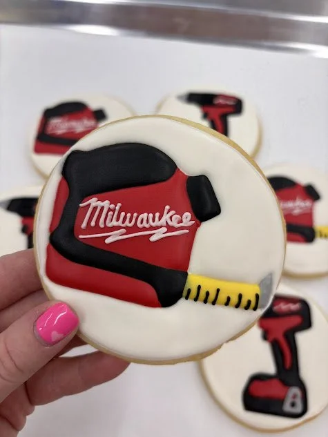 Cookies decorated with power tools and Milwaukee branding, featuring a red and black drill and a tape measure