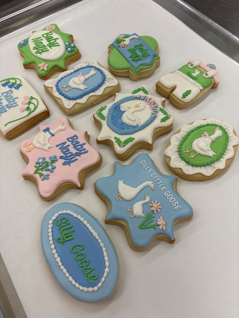 Assorted cookies decorated with swan and body positivity themes, featuring swan images, flowers, and the phrases "Body Nice" and "Swan GOOSE."