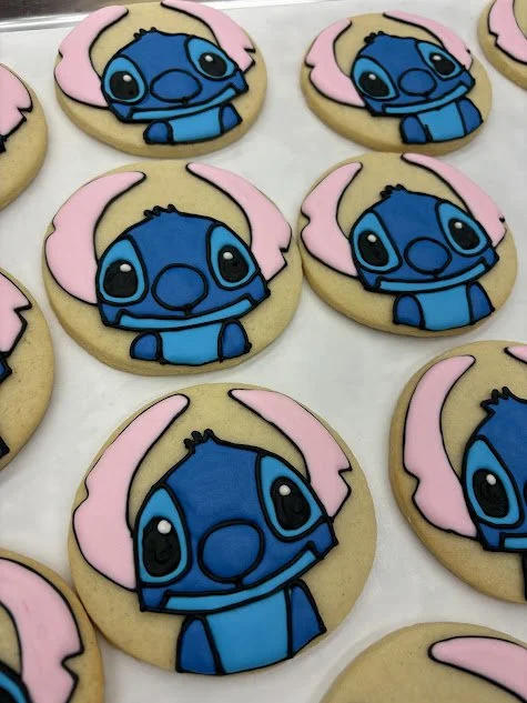 Cookies decorated with Stitch from Lilo & Stitch, featuring blue icing for Stitch's face and ears, and pink icing for his ears outline.