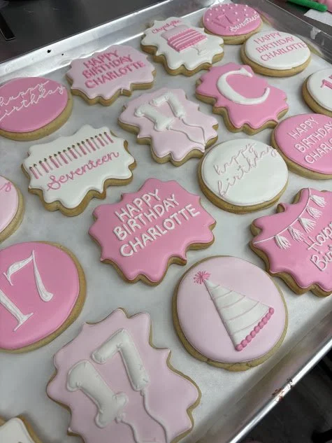 Decorated birthday cookies in pink and white with messages like 'Happy Birthday Charlotte' and 'Seventeener,' featuring candles, a party hat, and the number 17.