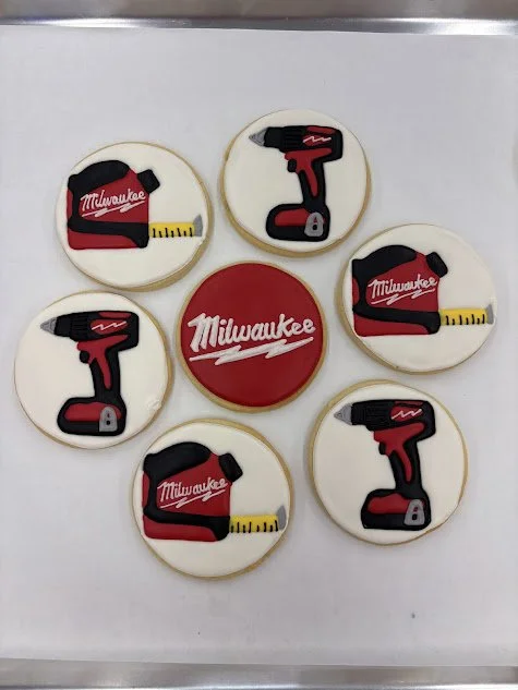 Cookies decorated with Milwaukee tools and logo, including tape measure, drill, and logo