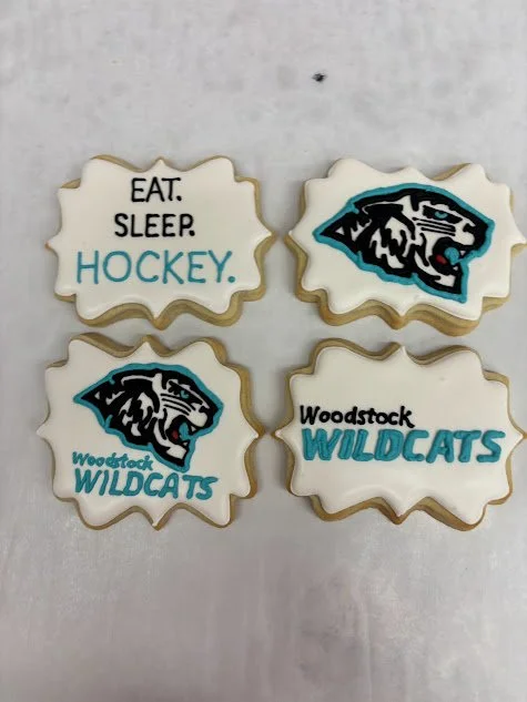 Four cookies with hockey and wildcats theme. Two cookies display the Wildcats logo, and two cookies contain the phrases "EAT. SLEEP. HOCKEY" and "Woodstock WILDCATS."